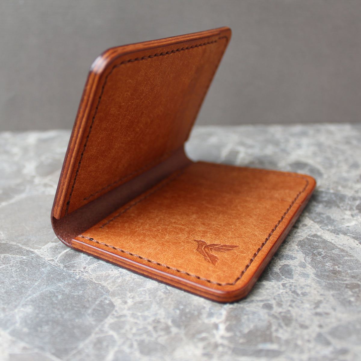 A brown leather card holder or wallet standing open on a gray marble surface against a gray background.