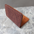 A brown textured leather card holder or wallet standing open on a gray marble surface.
