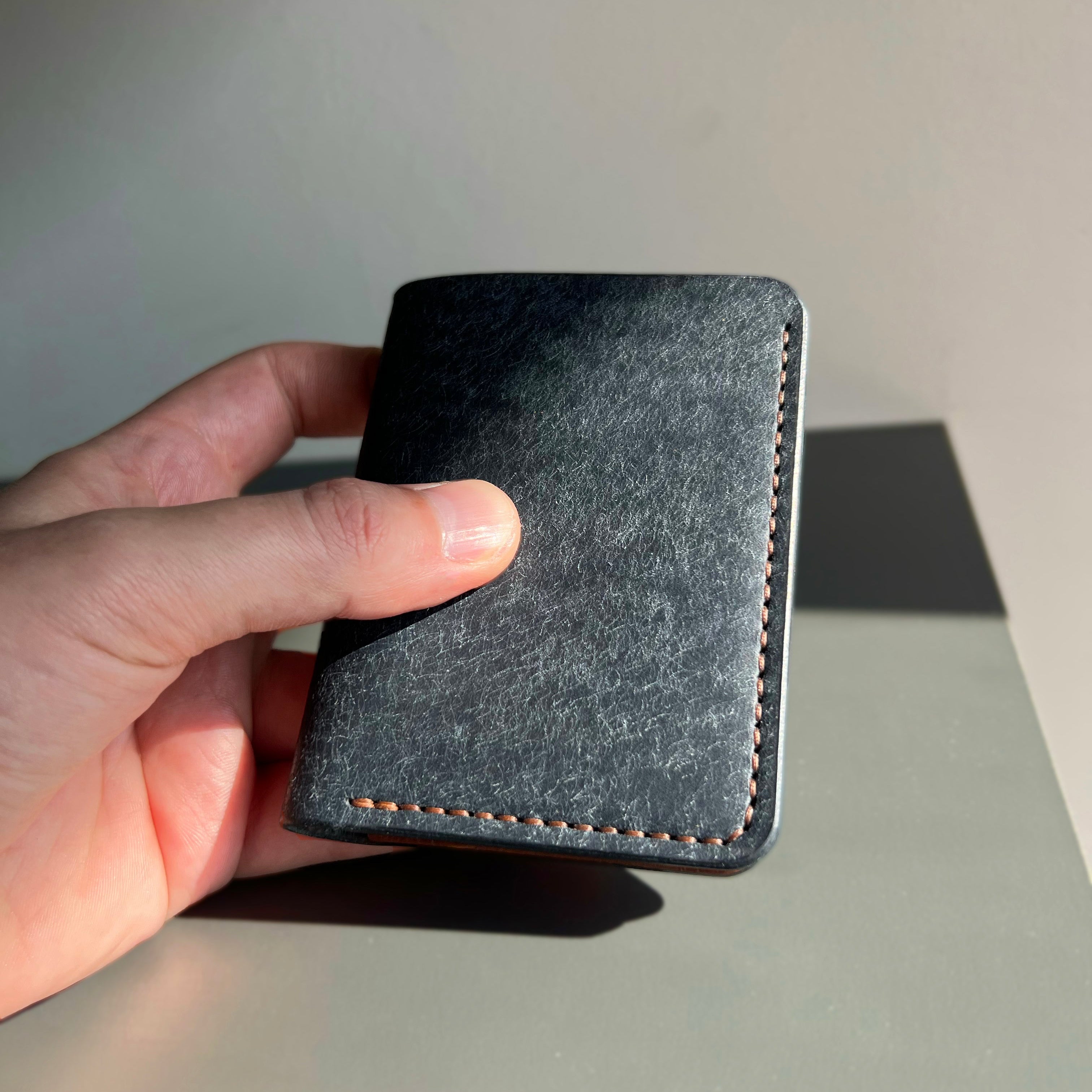 Hand holding a dark gray wallet against a neutral background