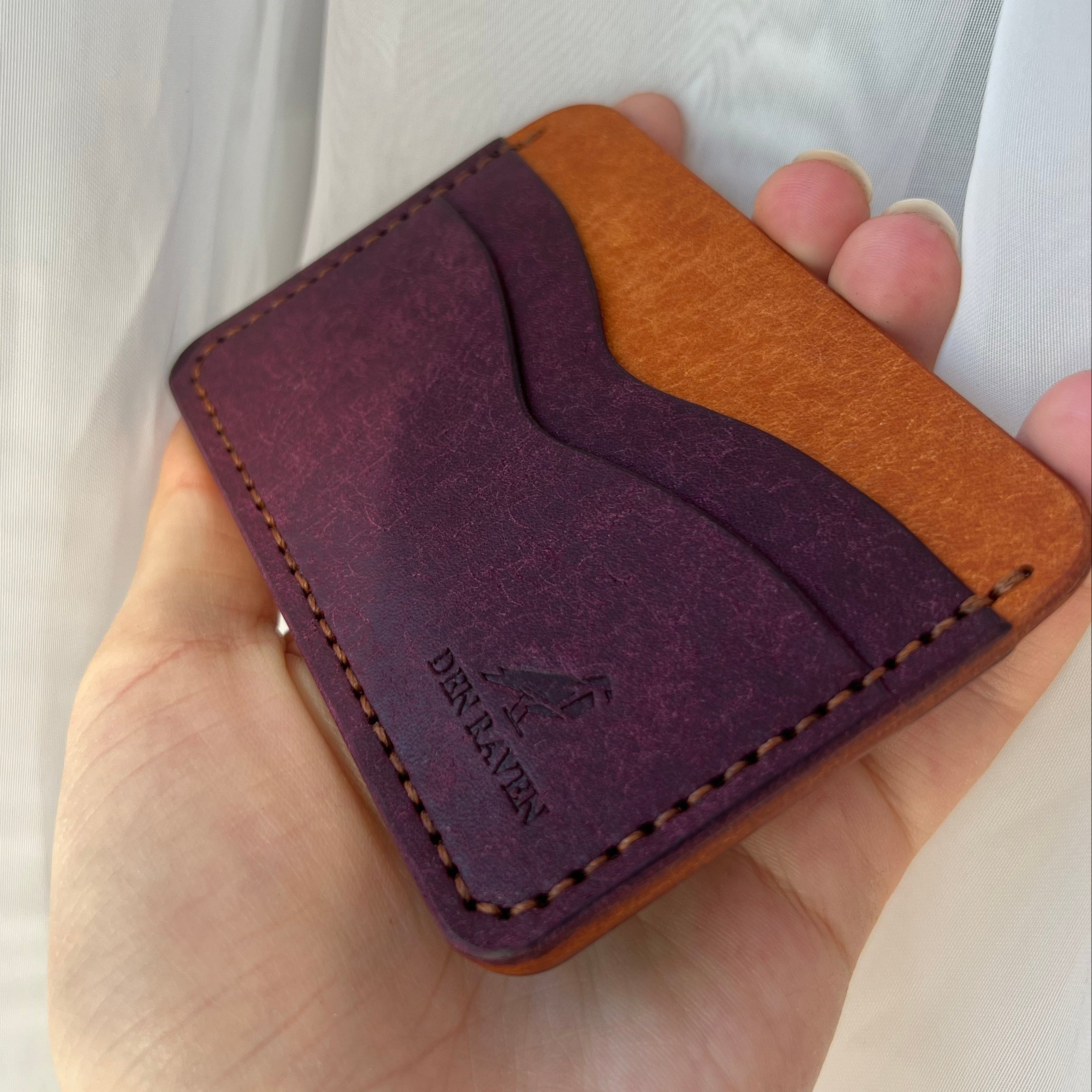 Hand holding a two-tone leather wallet with visible brand name.