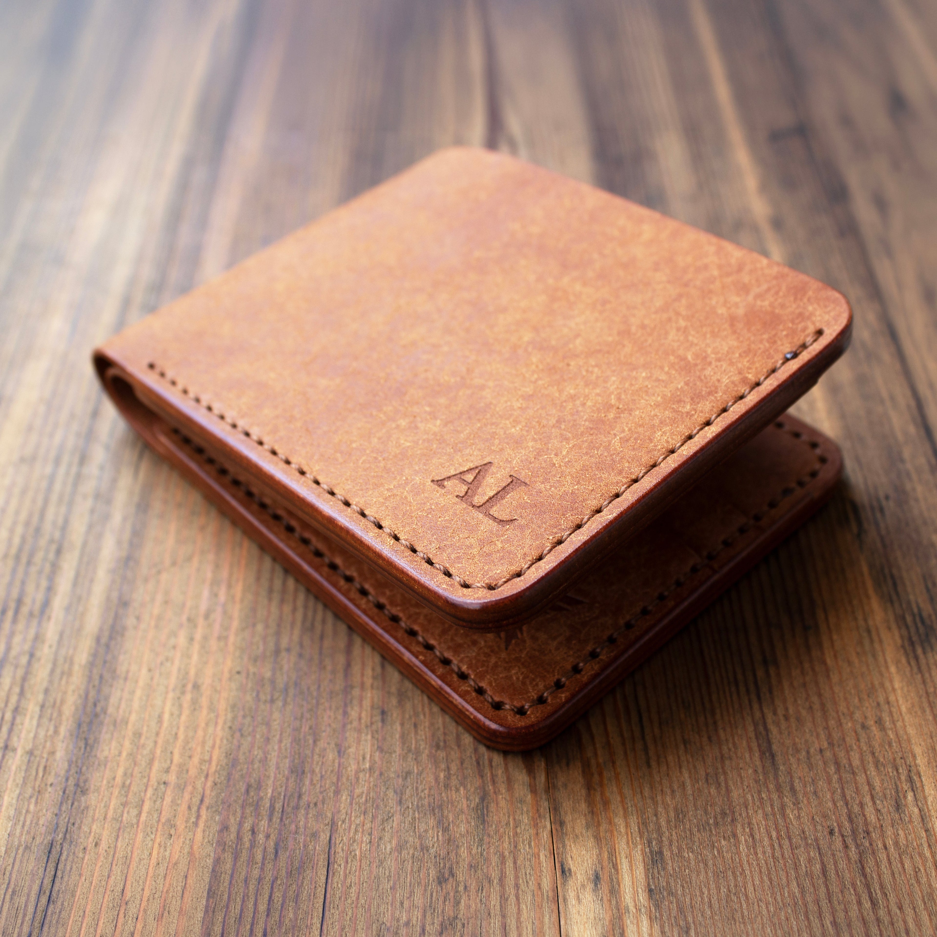 Brown leather wallet with initials on a wooden surface