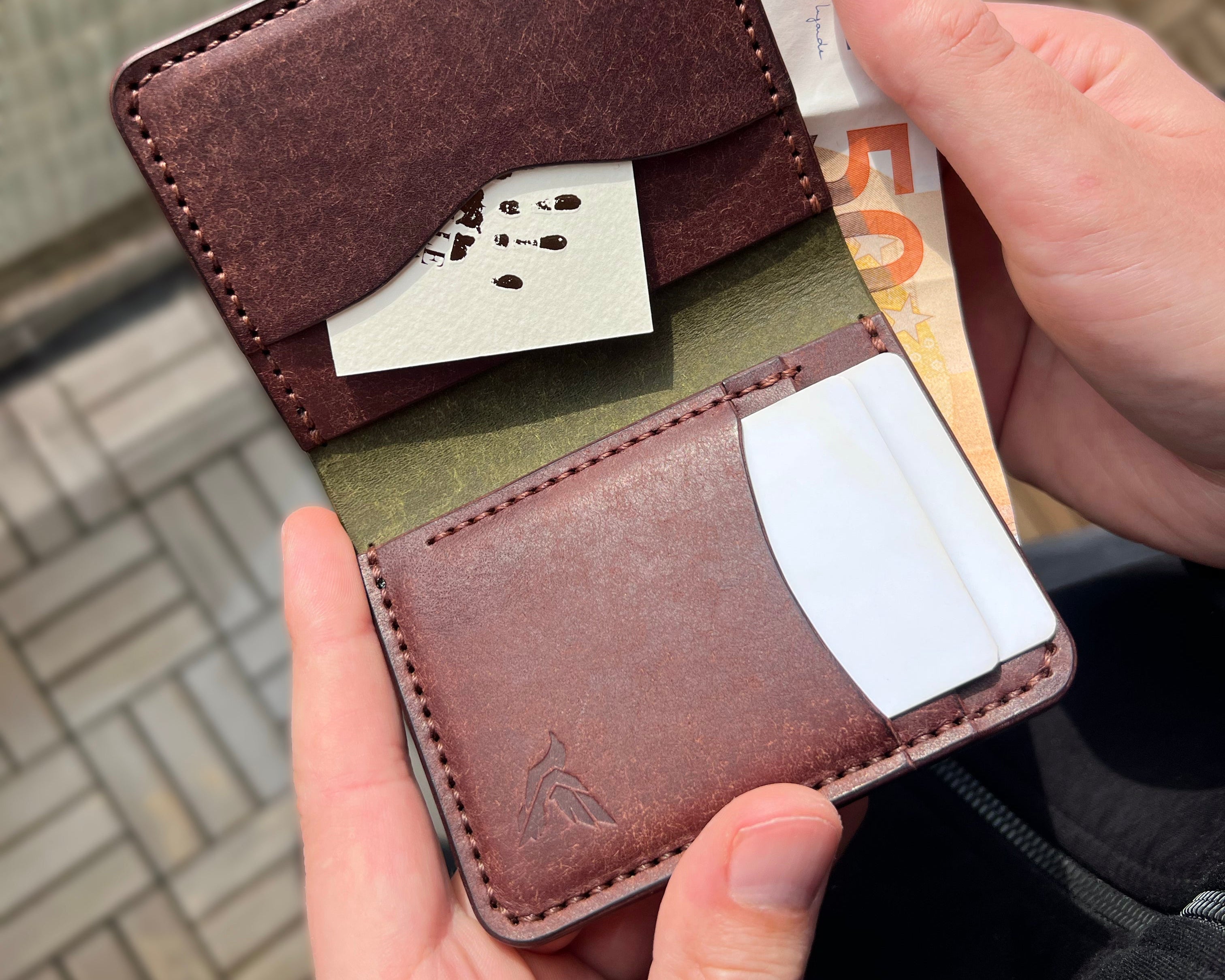 Brown leather wallet with card slots held by a person against a blurred background