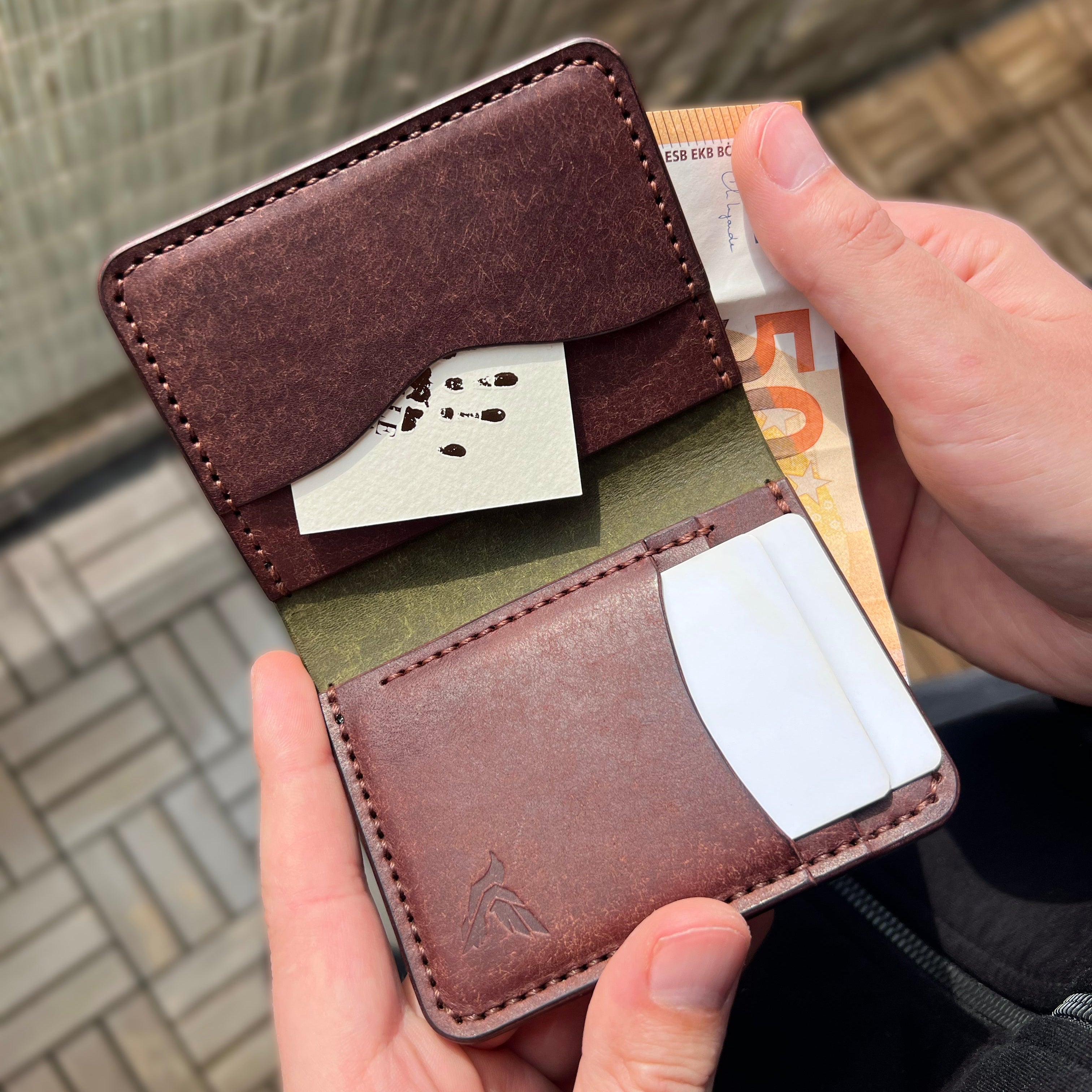 Brown leather wallet with card slots held by a person against a blurred background