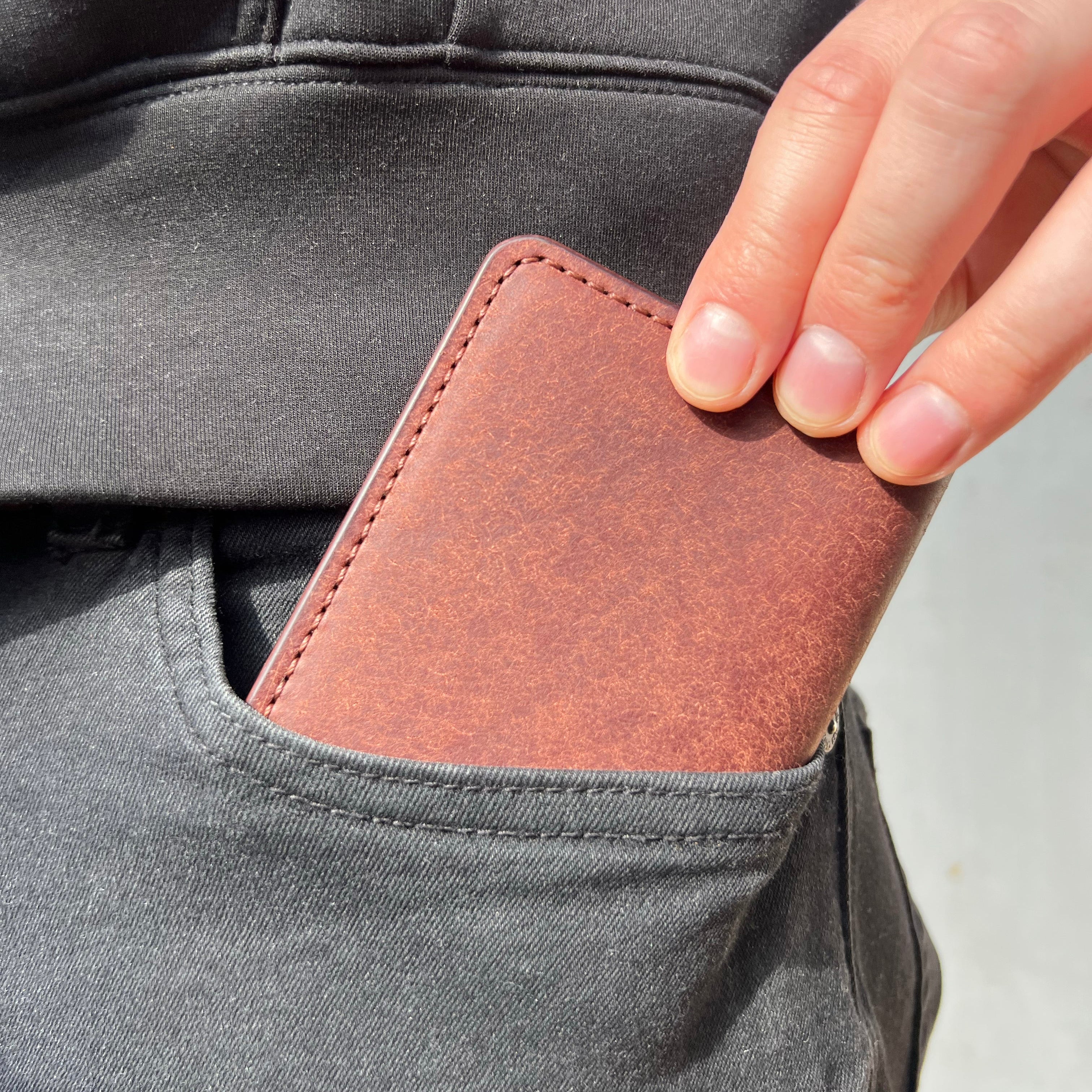 Brown leather wallet being inserted into a gray pocket.