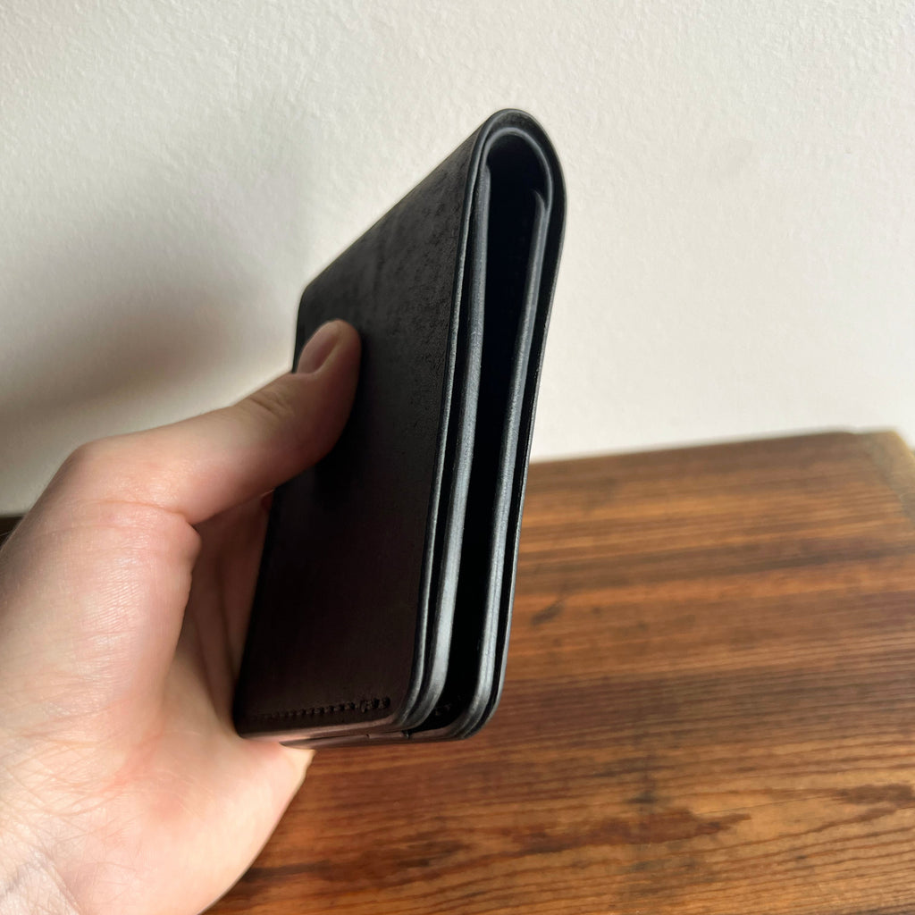 Hand holding a black wallet on a wooden surface with a white background