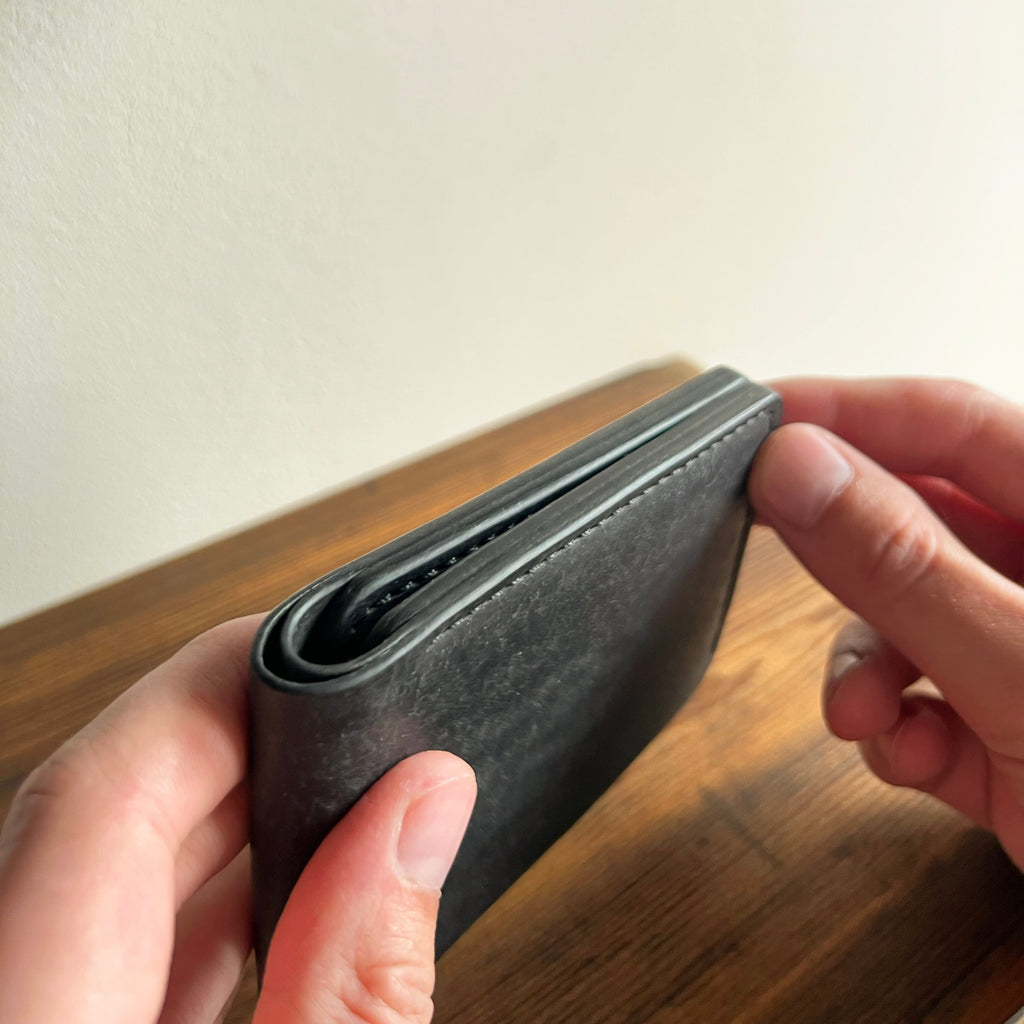 Person holding a black wallet against a neutral background