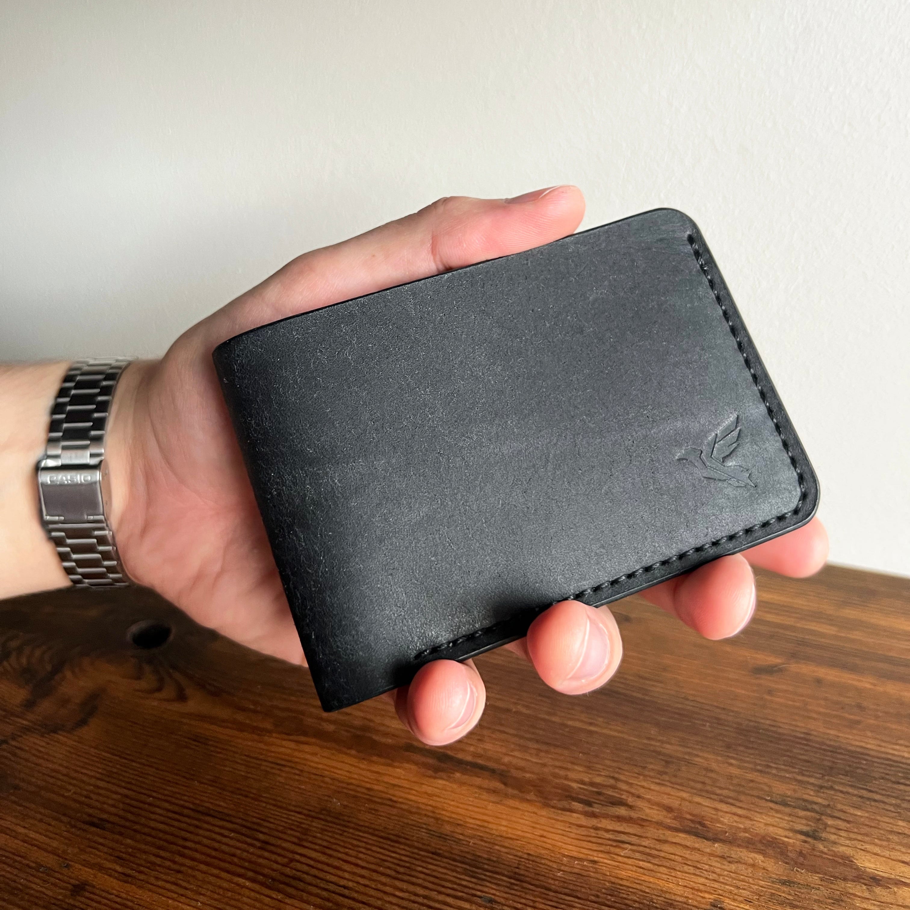 Hand holding a black leather wallet on a wooden surface with a neutral background