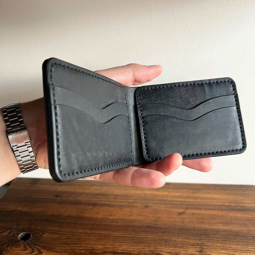 Hand holding an open black leather wallet on a wooden surface with a neutral background