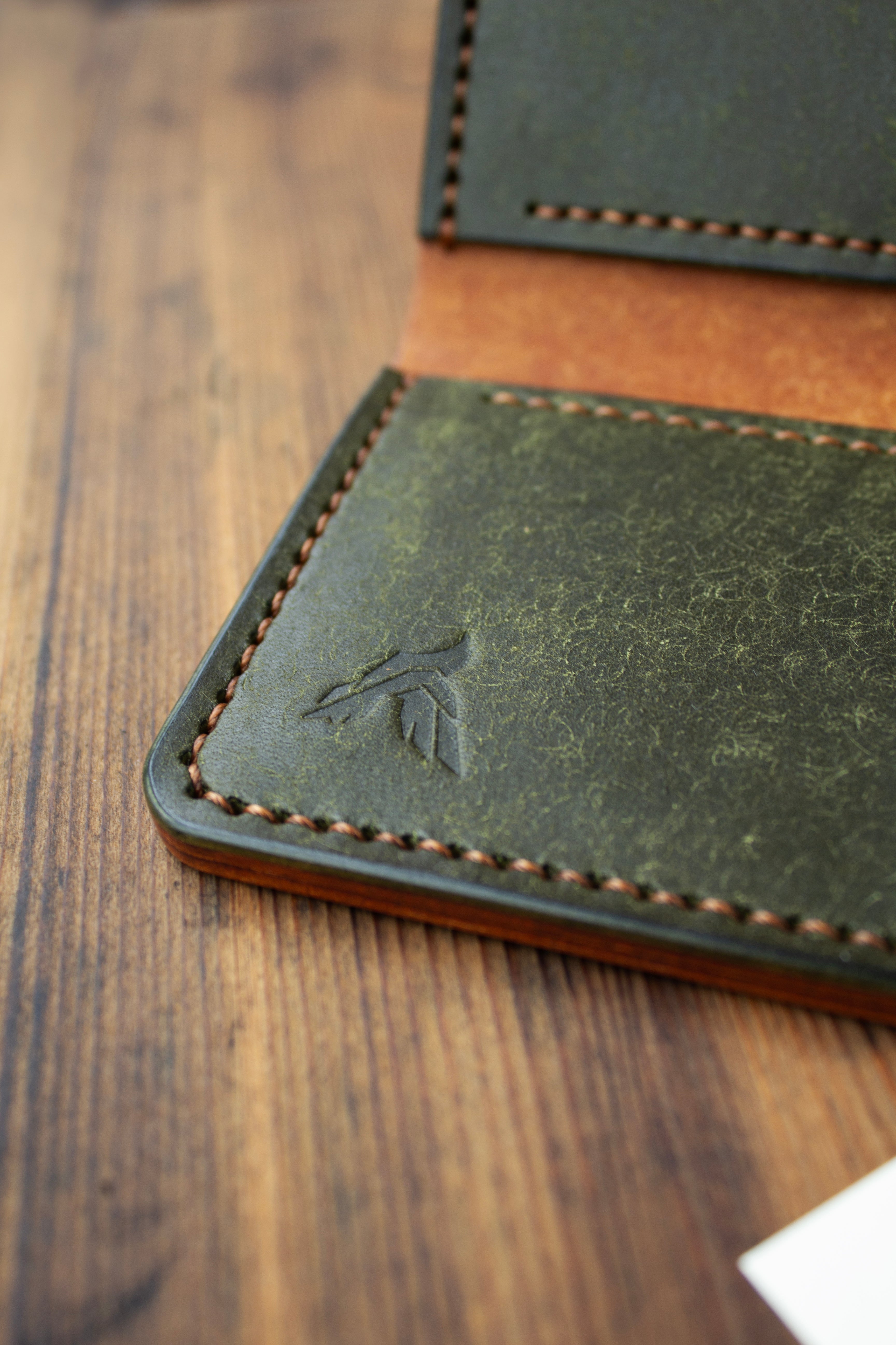 Close-up of a green leather wallet with brown stitching on a wooden surface
