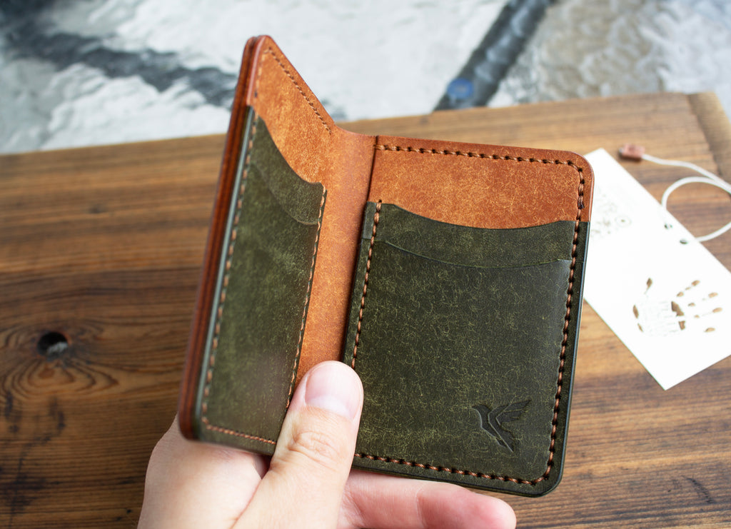 Brown and green leather wallet held by a hand on a wooden surface with a blurred background