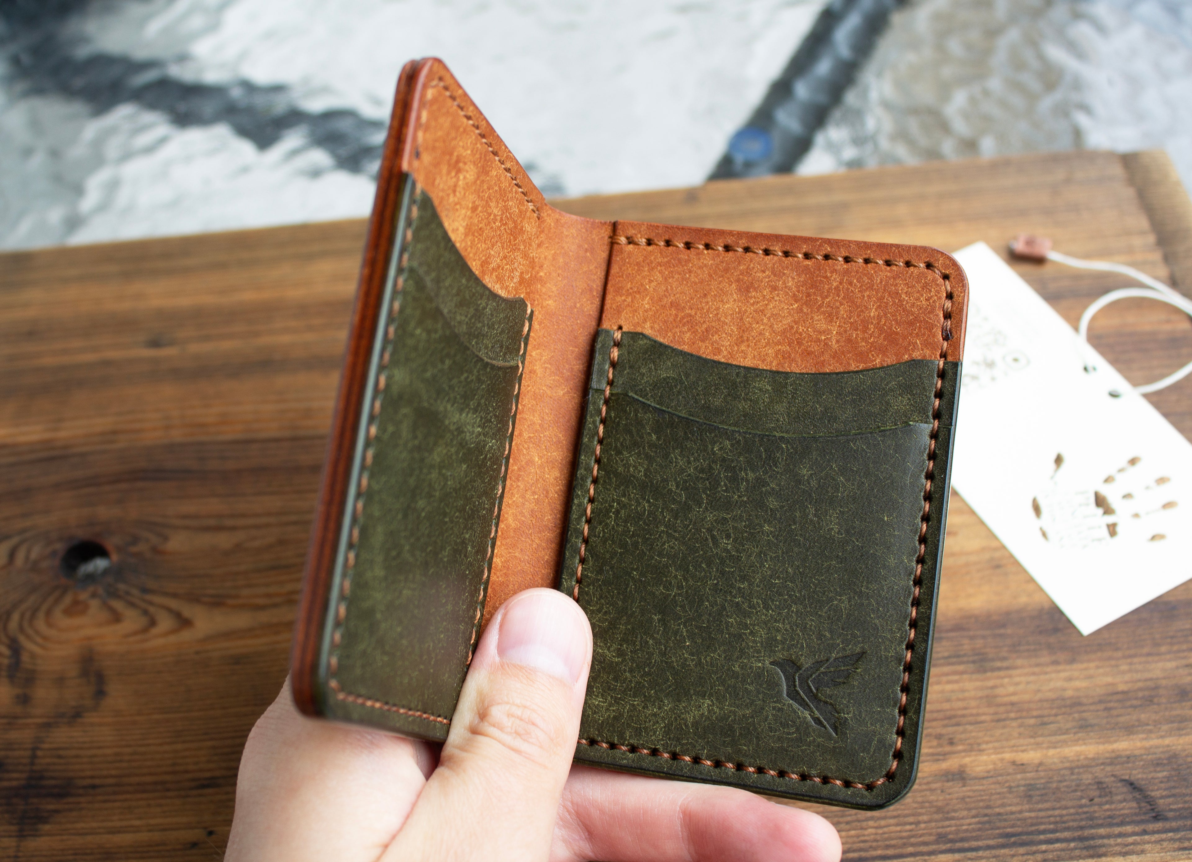 Brown and green leather wallet held by a hand on a wooden surface with a blurred background