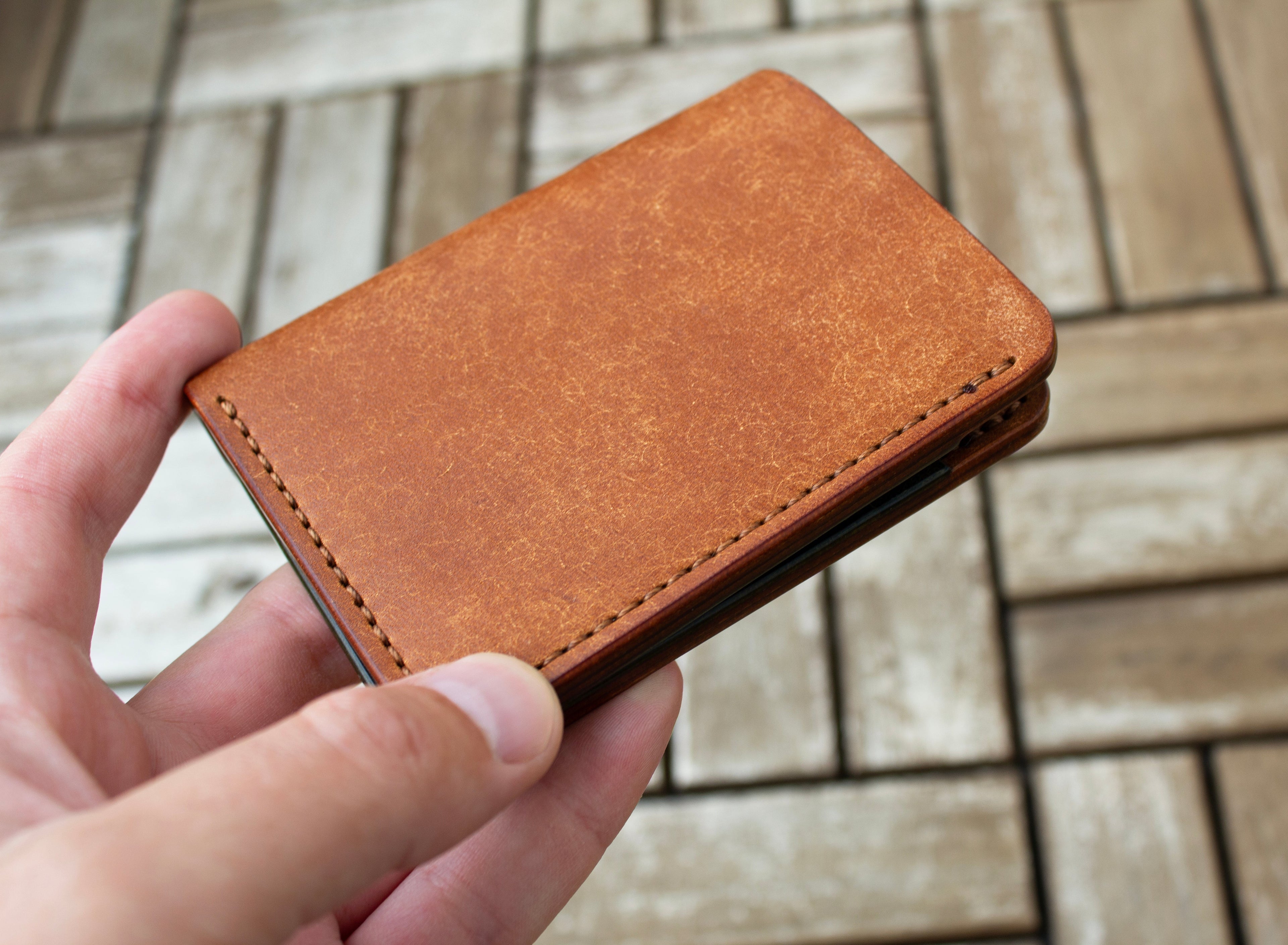 Brown leather wallet held in a hand on a wooden surface