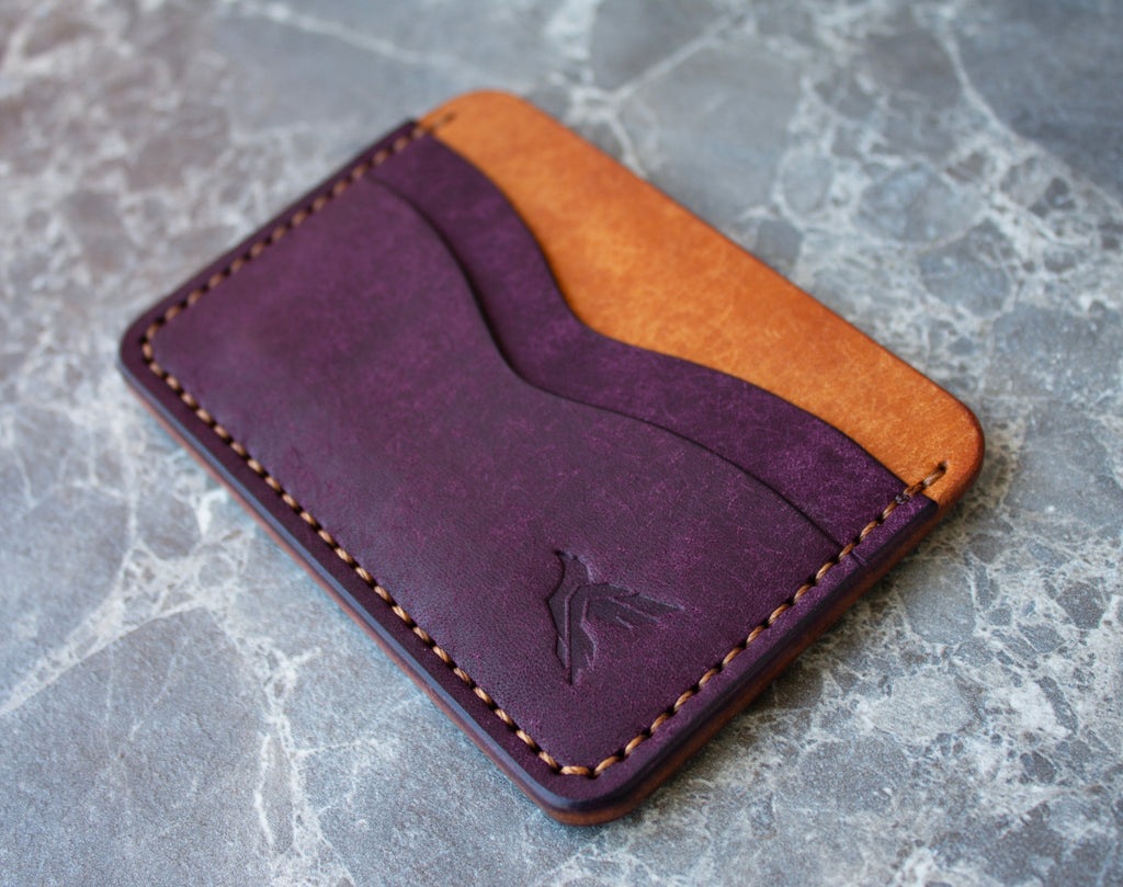 Two-tone purple and orange leather wallet on a gray marble surface