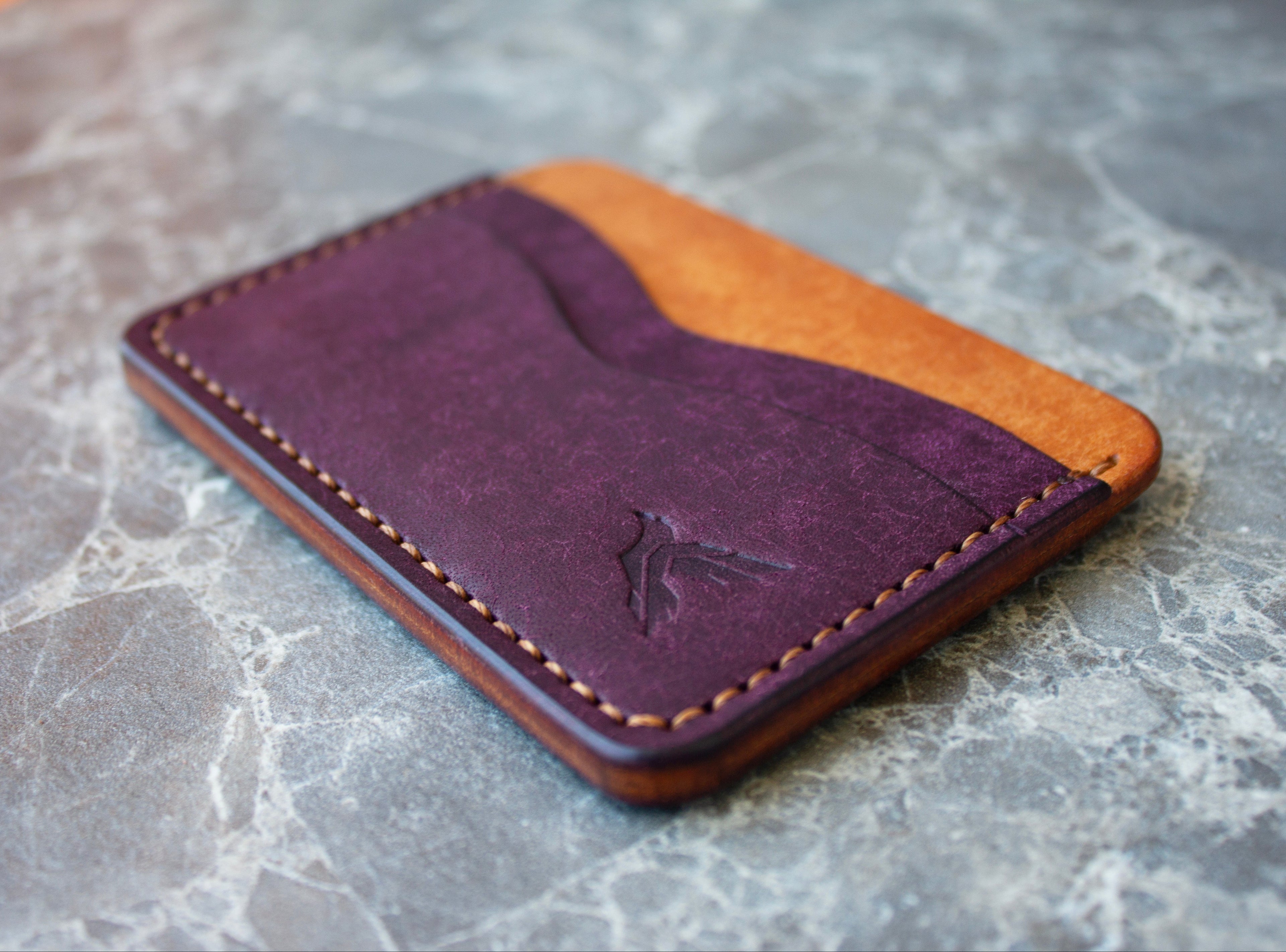 Two-tone purple and orange leather wallet on a gray marble surface