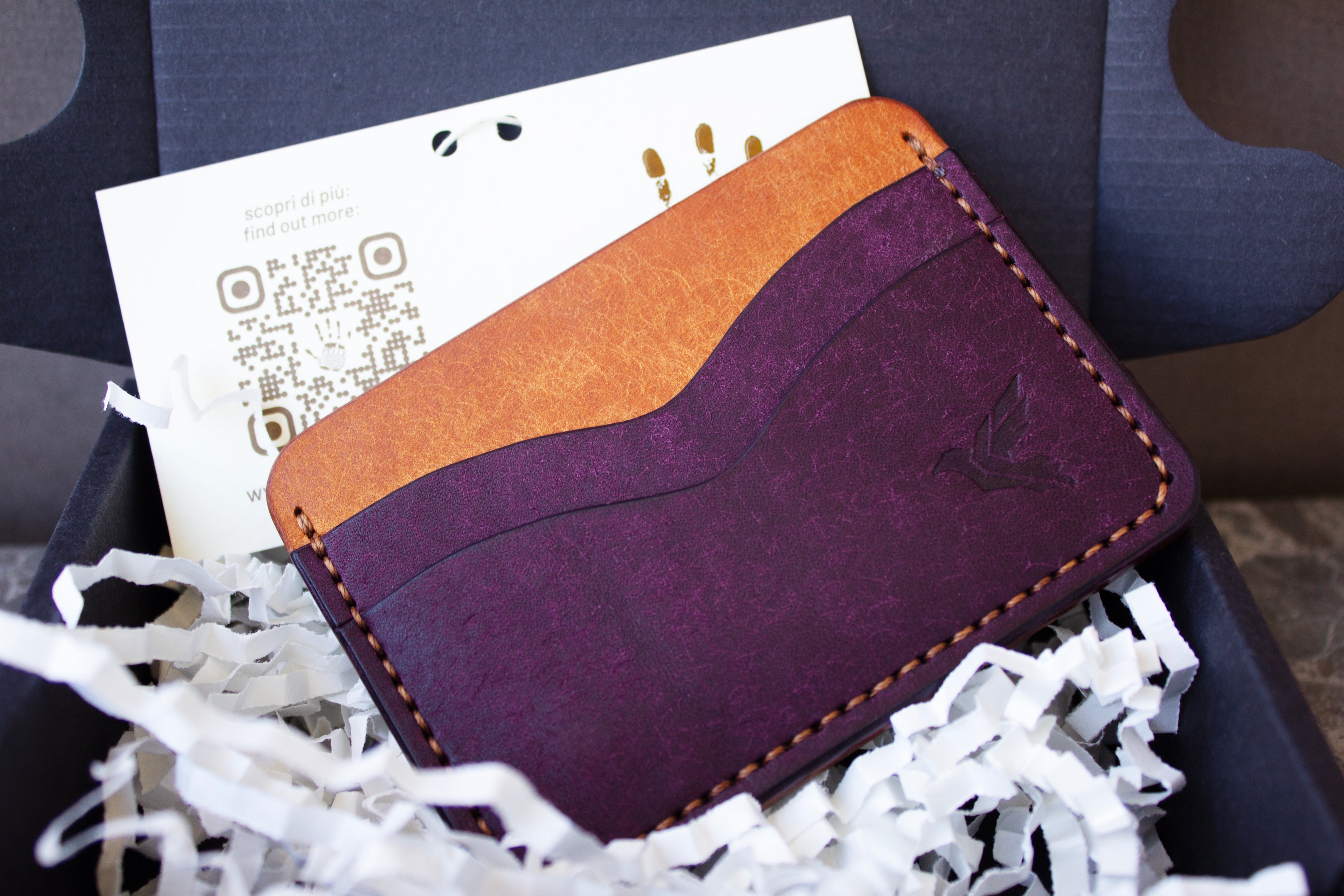 Purple and orange leather wallet with a QR code on a white card, placed in white shredded paper.