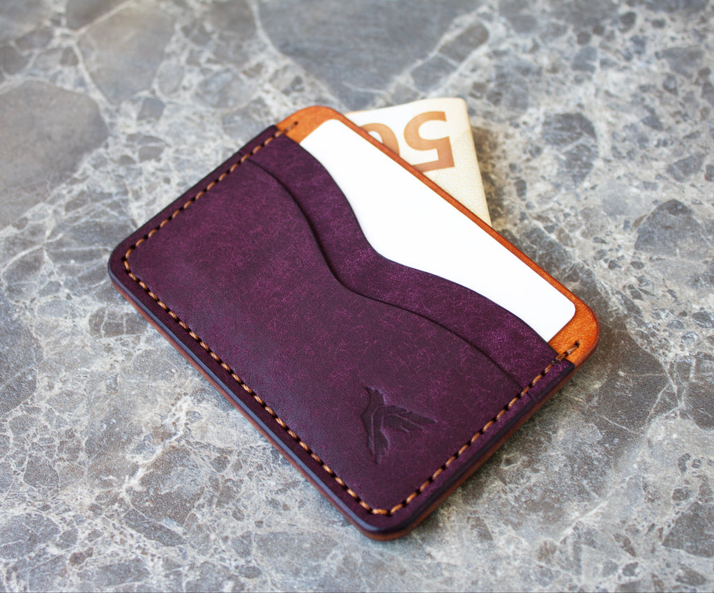Purple leather cardholder with orange stitching on a gray stone surface