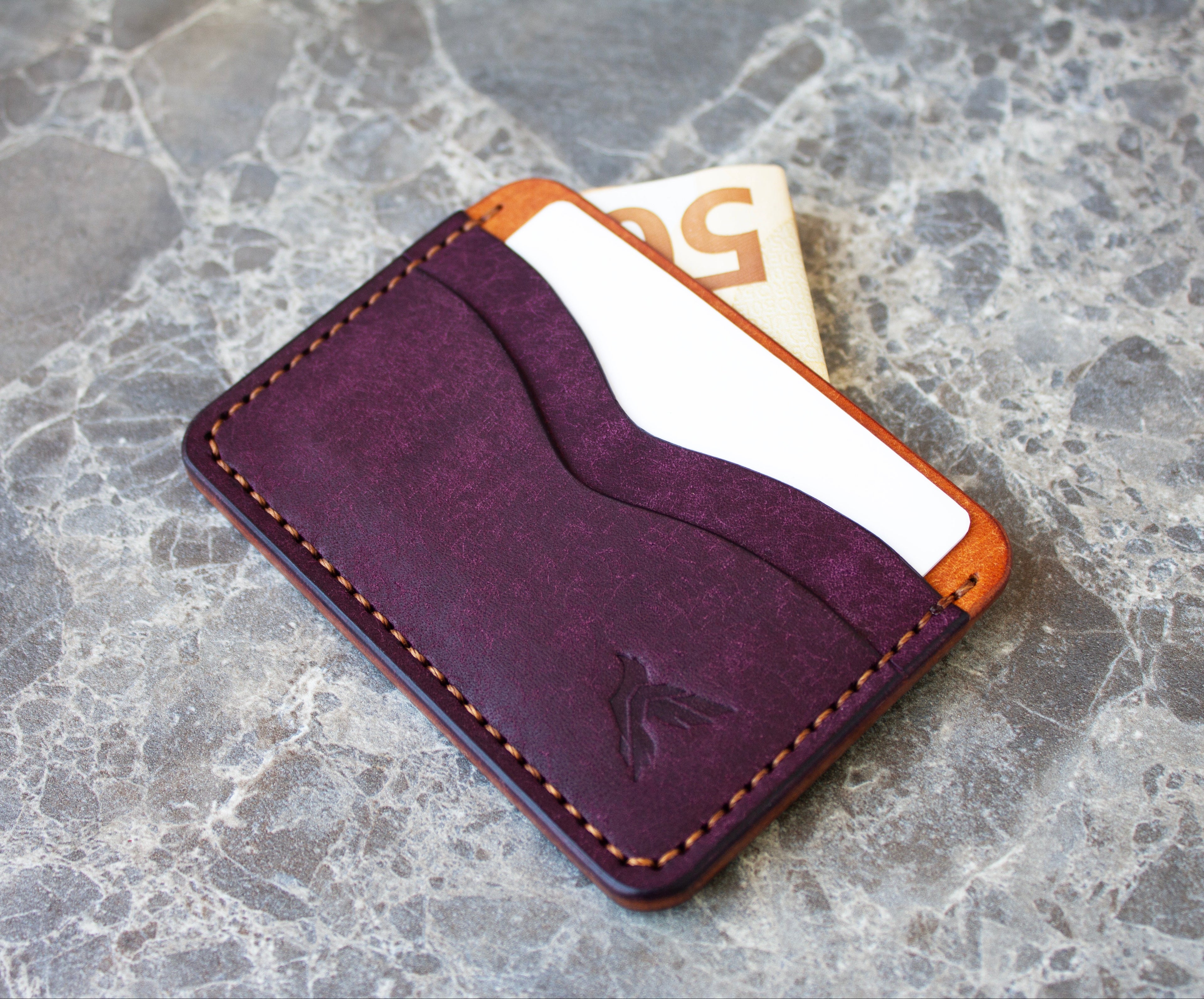 Purple leather cardholder with orange stitching on a gray stone surface