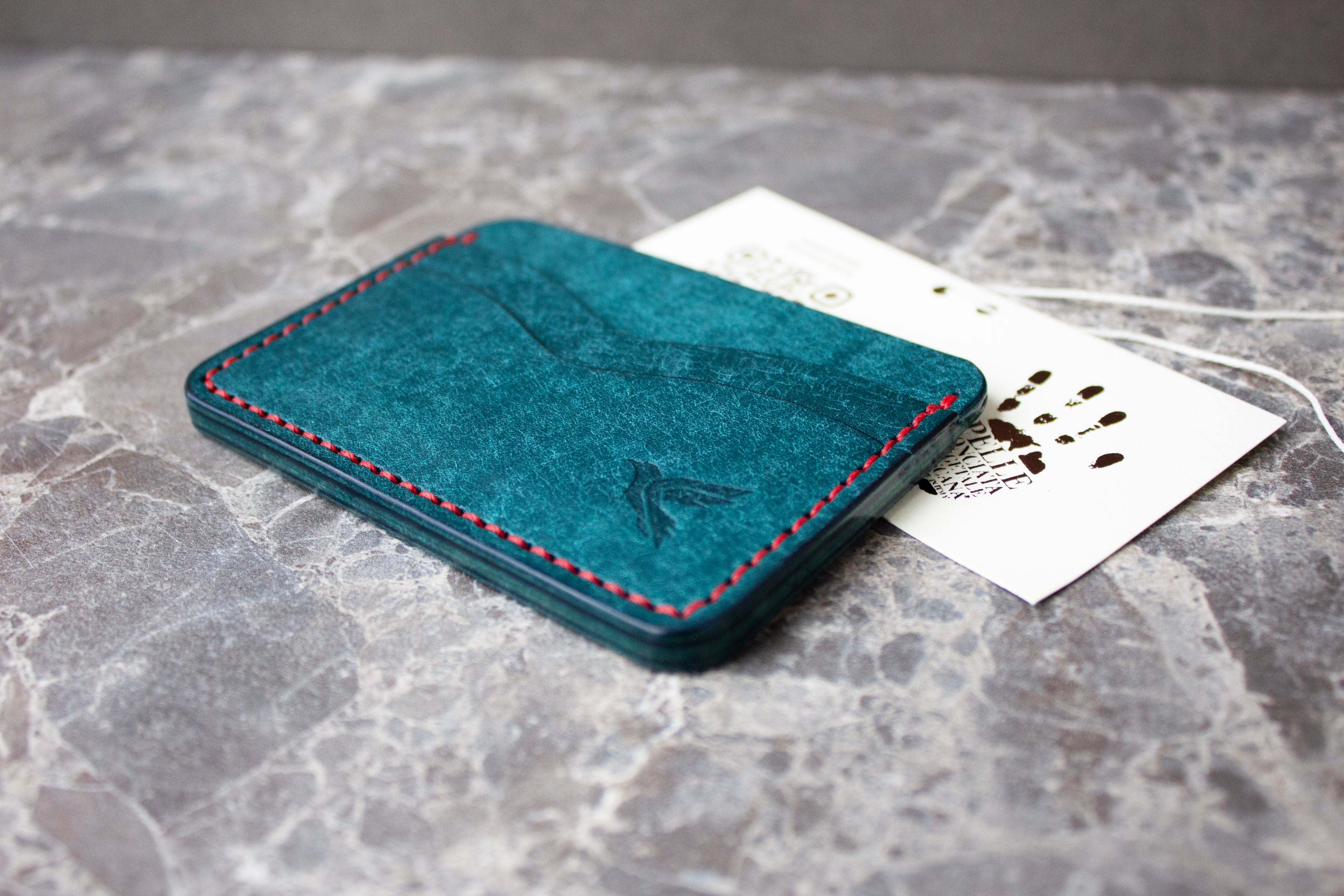 Blue leather cardholder with red stitching on a marble surface