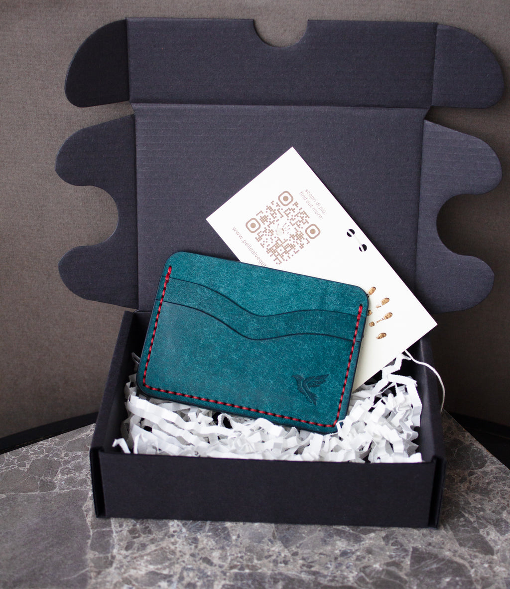 Teal cardholder with red stitching in a box with tissue paper