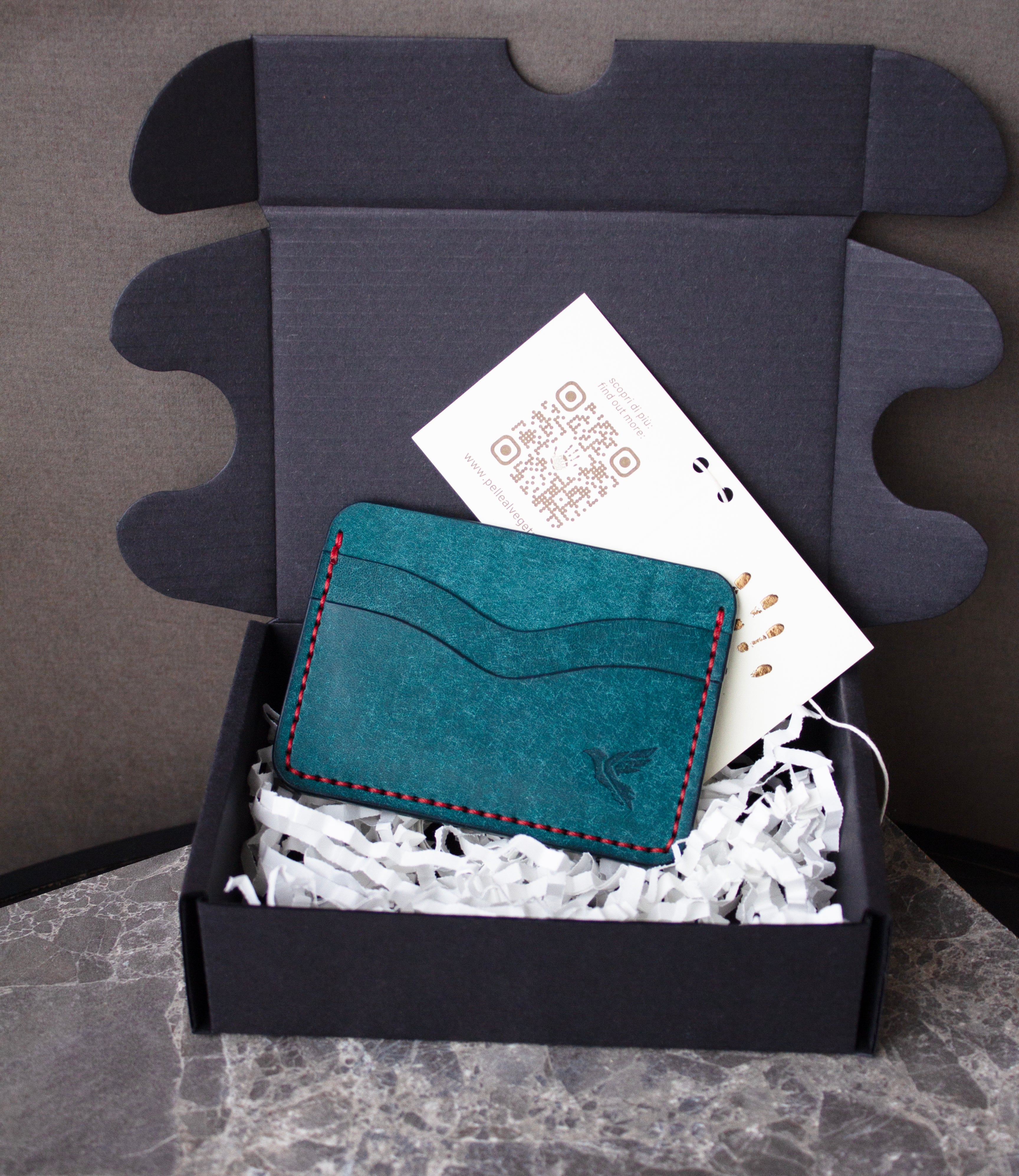 Teal cardholder with red stitching in a box with tissue paper