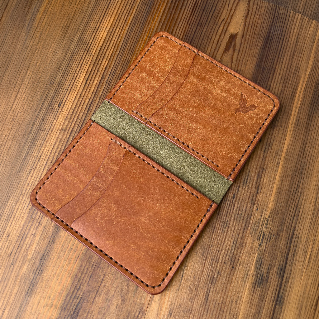 Brown leather wallet with green accent on a wooden surface
