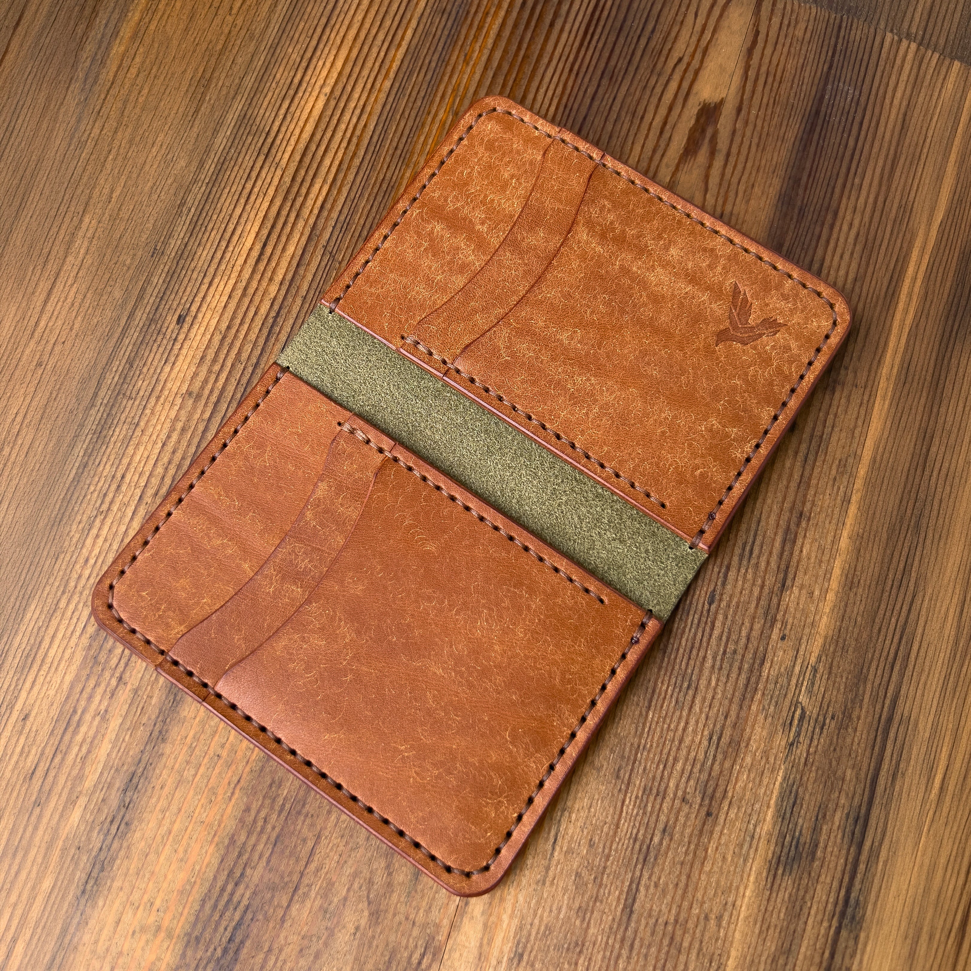 Brown leather wallet with green accent on a wooden surface