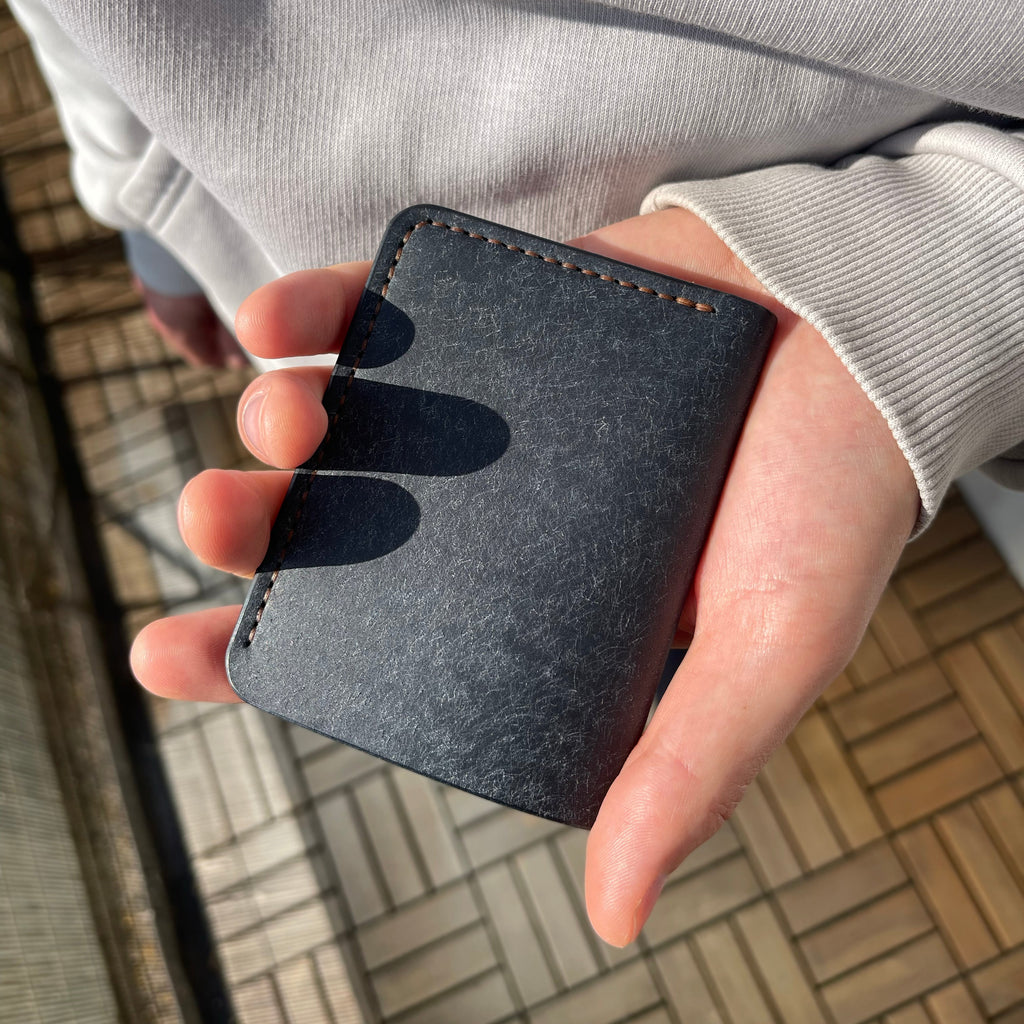 Hand holding a black leather wallet against a blurred outdoor background