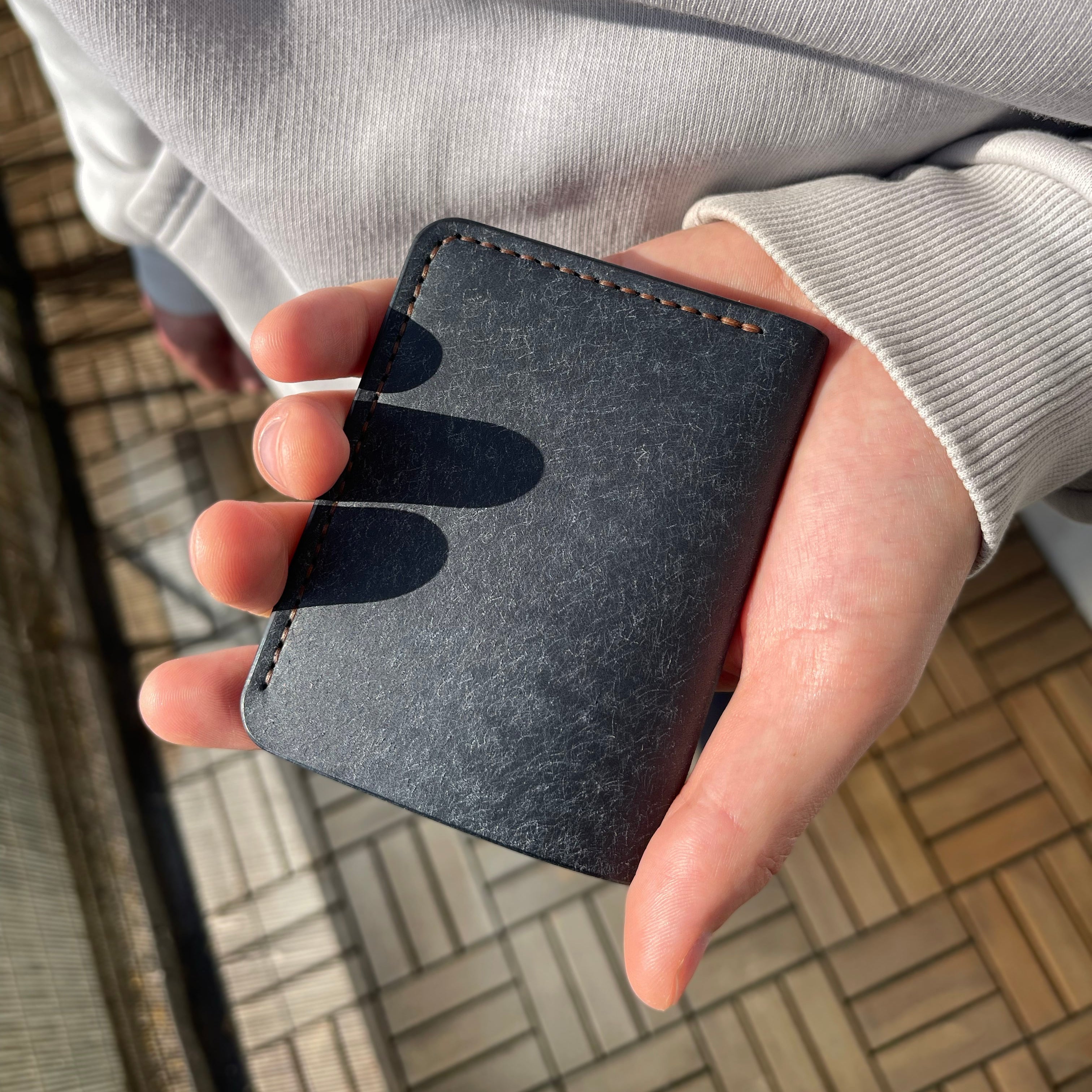 Hand holding a black leather wallet against a blurred outdoor background