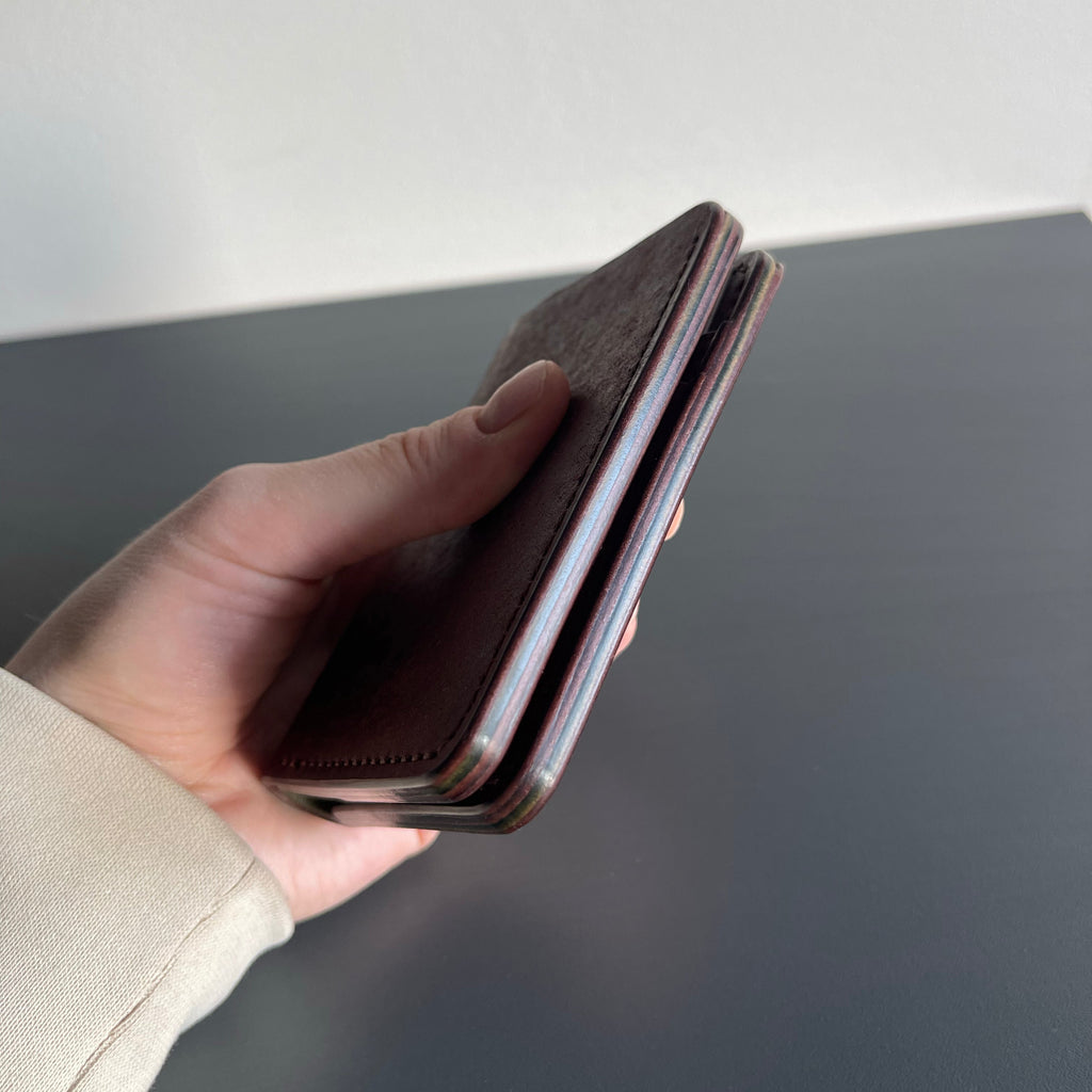 Hand holding a brown leather wallet against a neutral background