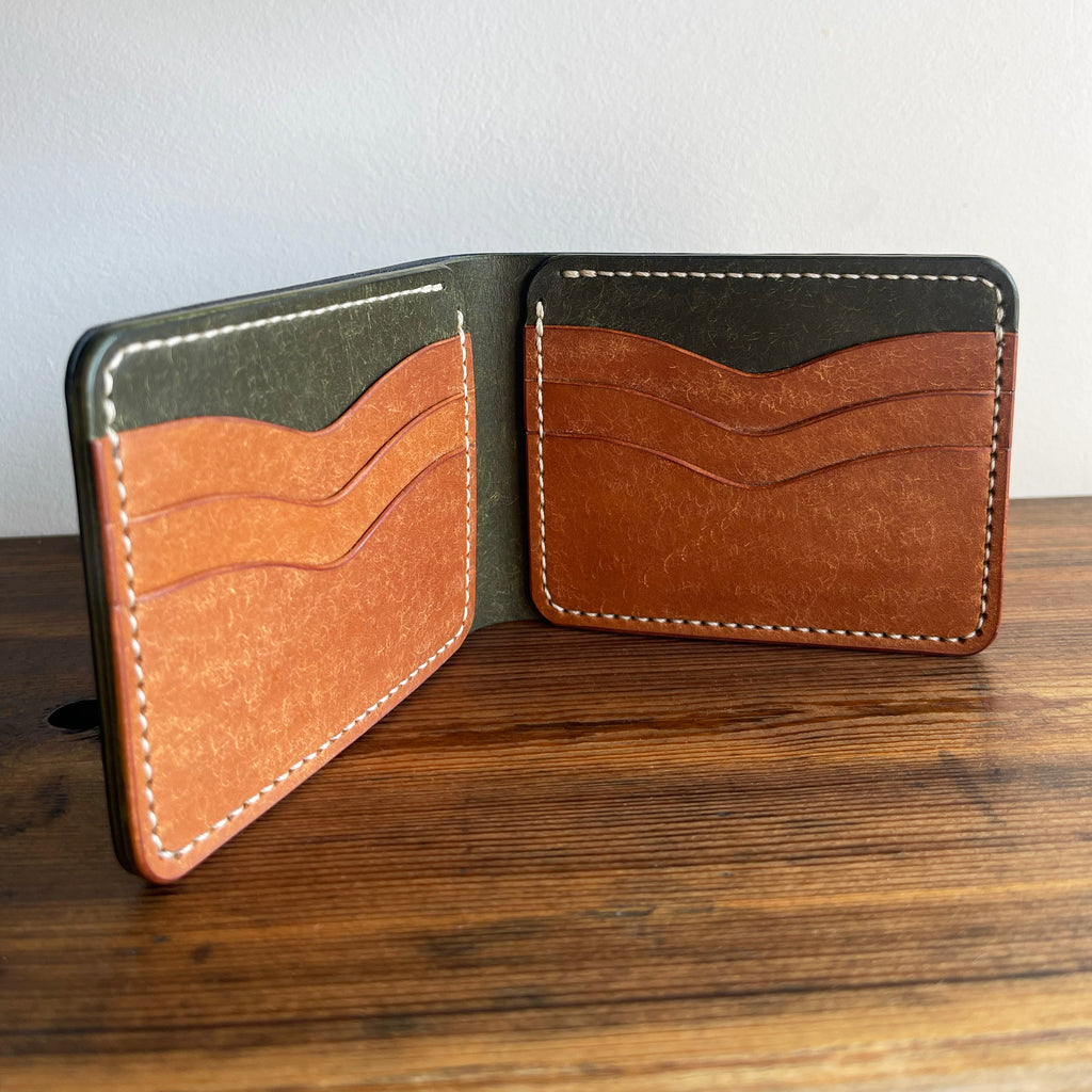Open leather wallet with brown and green sections on a wooden surface.