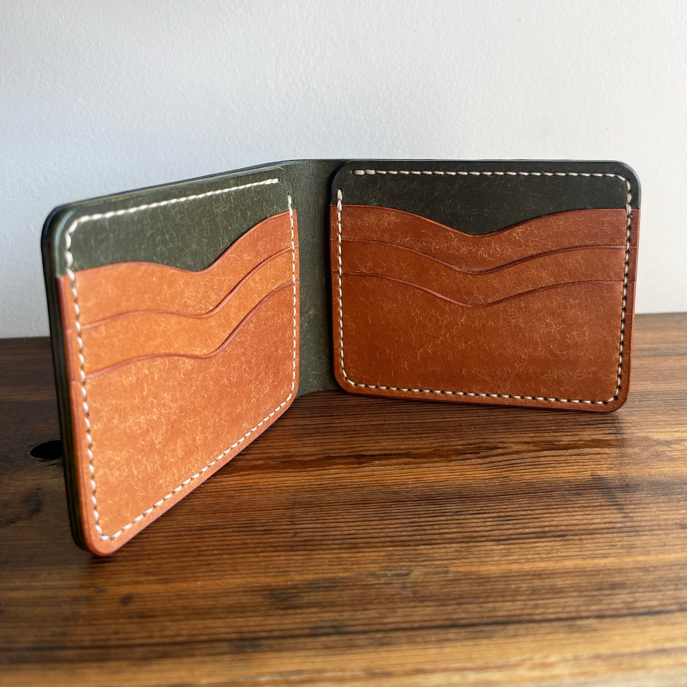 Open leather wallet with brown and green sections on a wooden surface.