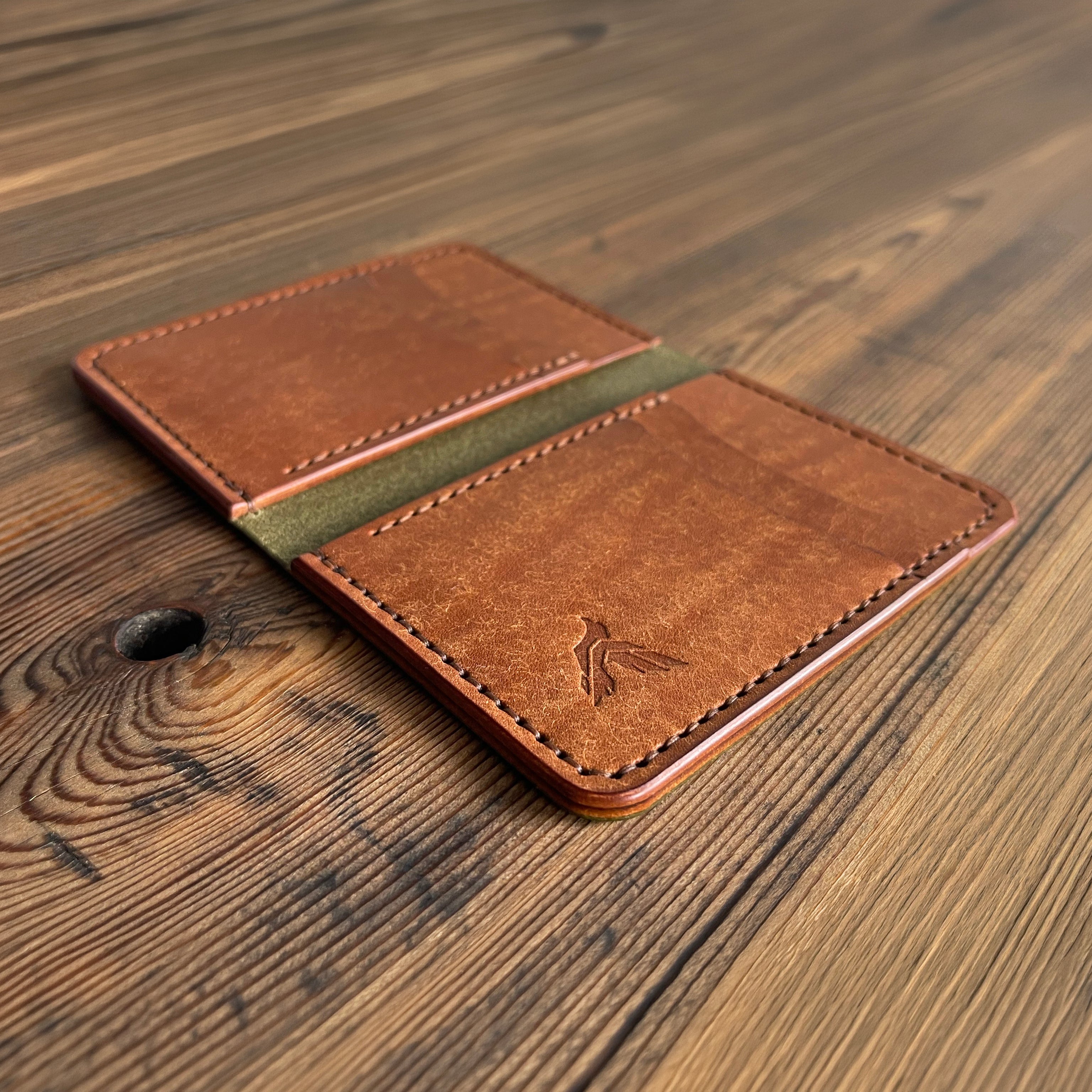 Brown leather wallet with green accent on a wooden surface