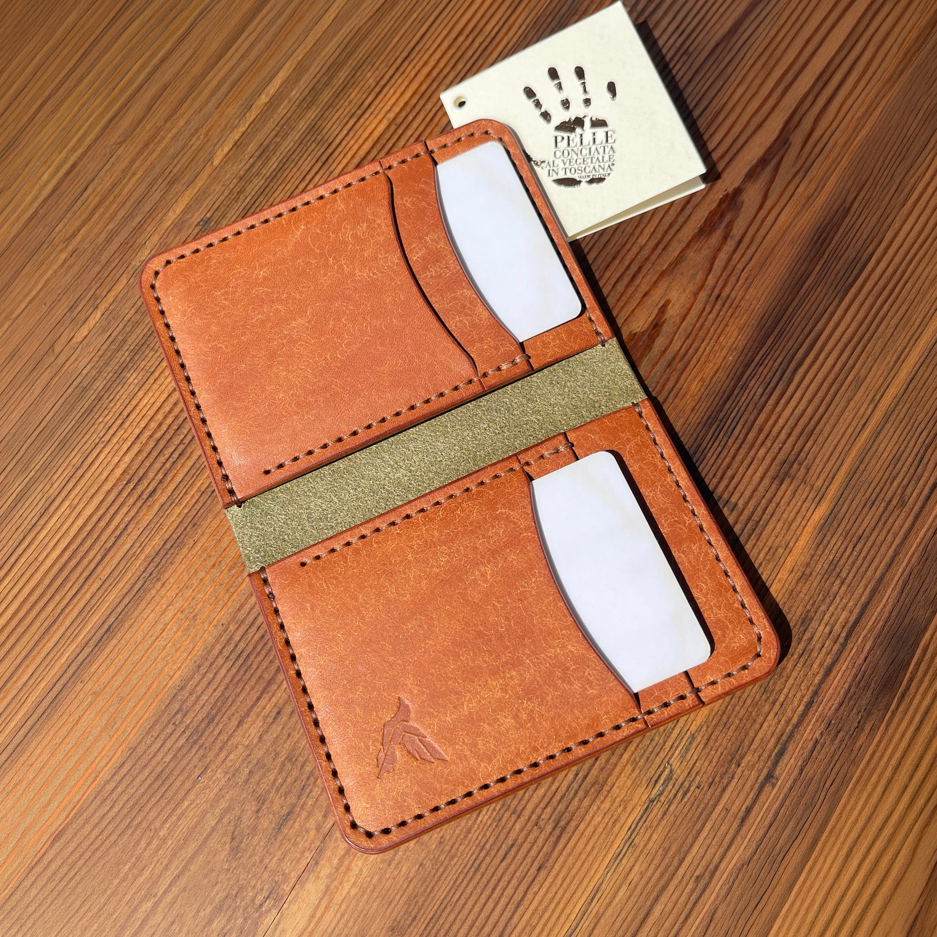 Brown leather wallet with green accent on a wooden surface, featuring a brand card.