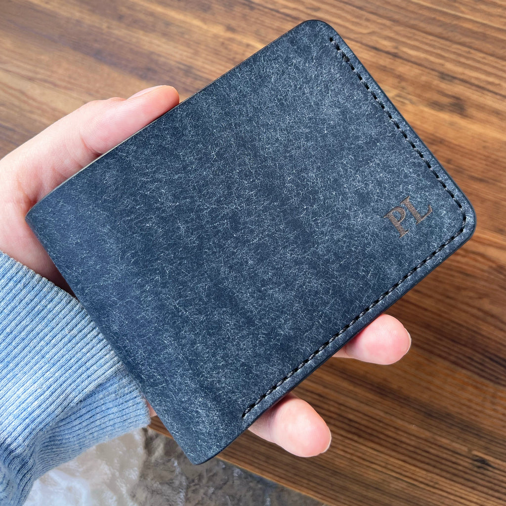 Hand holding a blue wallet with a brand logo on a wooden surface