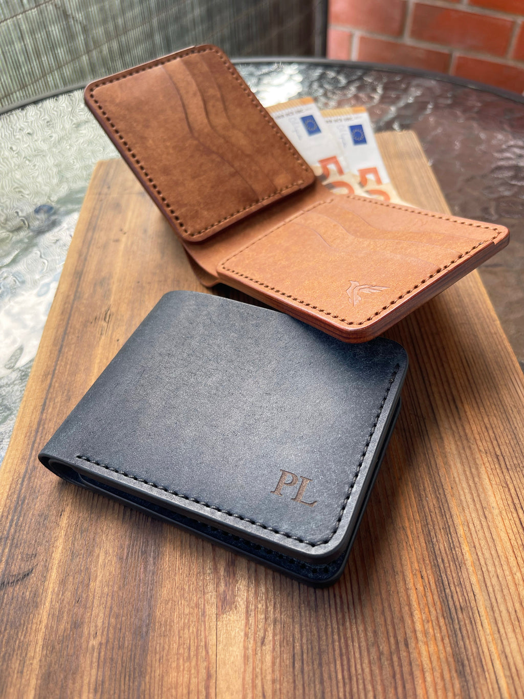 Three leather wallets in brown, black, and tan on a wooden surface.