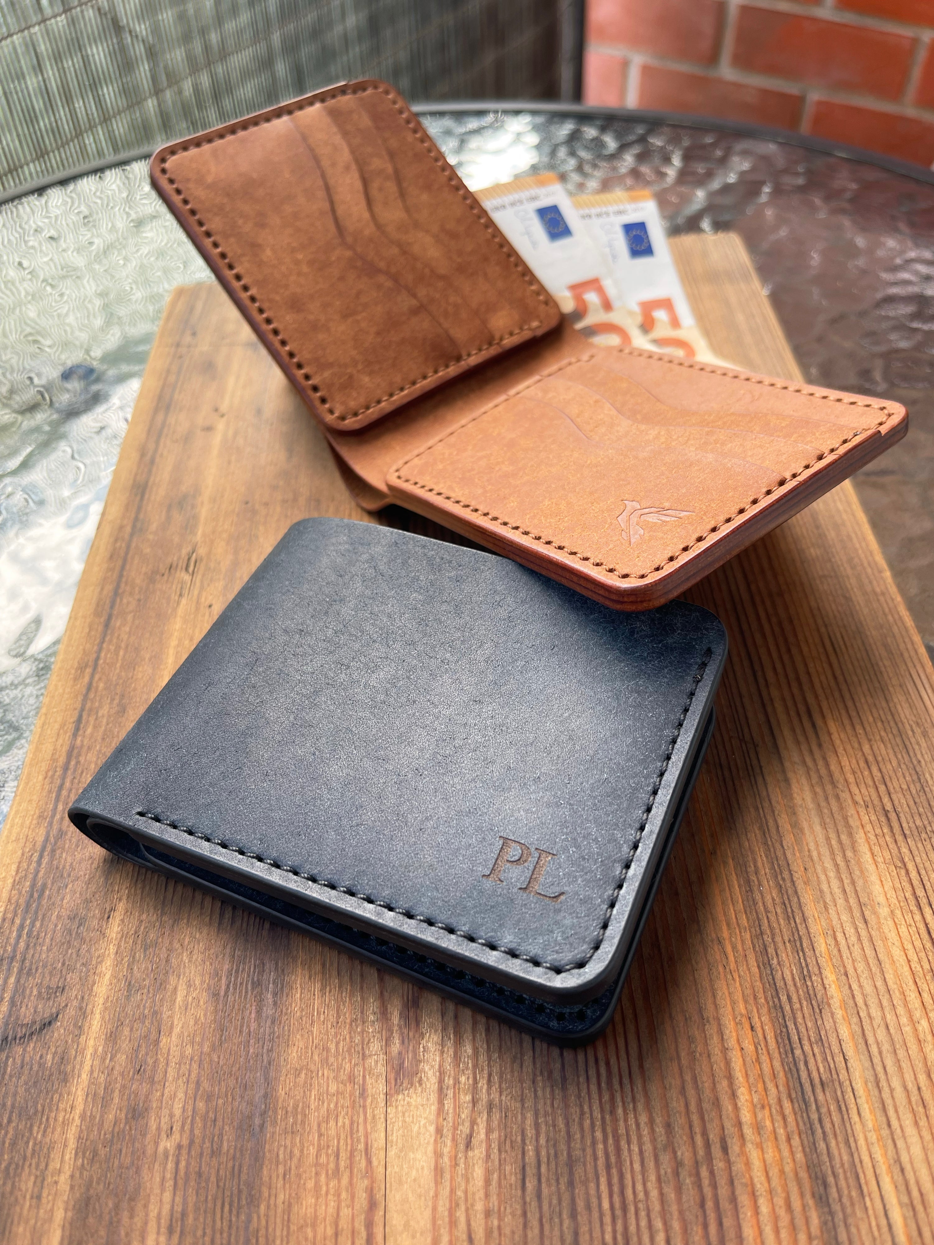 Three leather wallets in brown, black, and tan on a wooden surface.