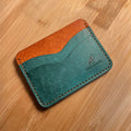 Two-tone leather cardholder with brown top section and teal bottom section on a wooden surface