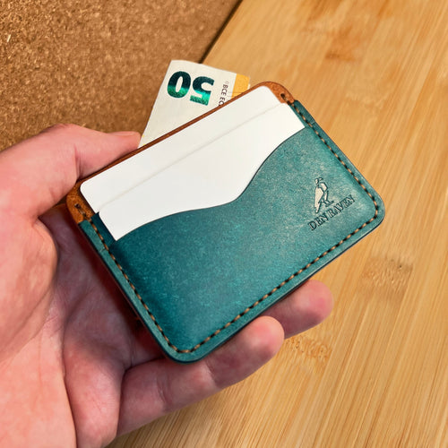 Hand holding a teal leather wallet with a card and money on a wooden surface