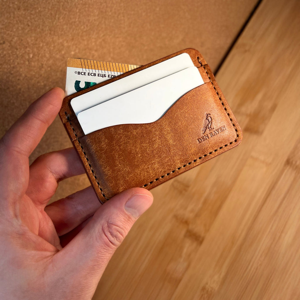 Brown leather cardholder with cards held by a hand on a wooden surface