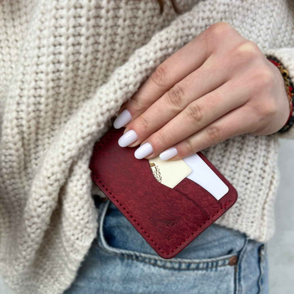 Person holding a maroon cardholder with a card inside, wearing a beige sweater and blue jeans.