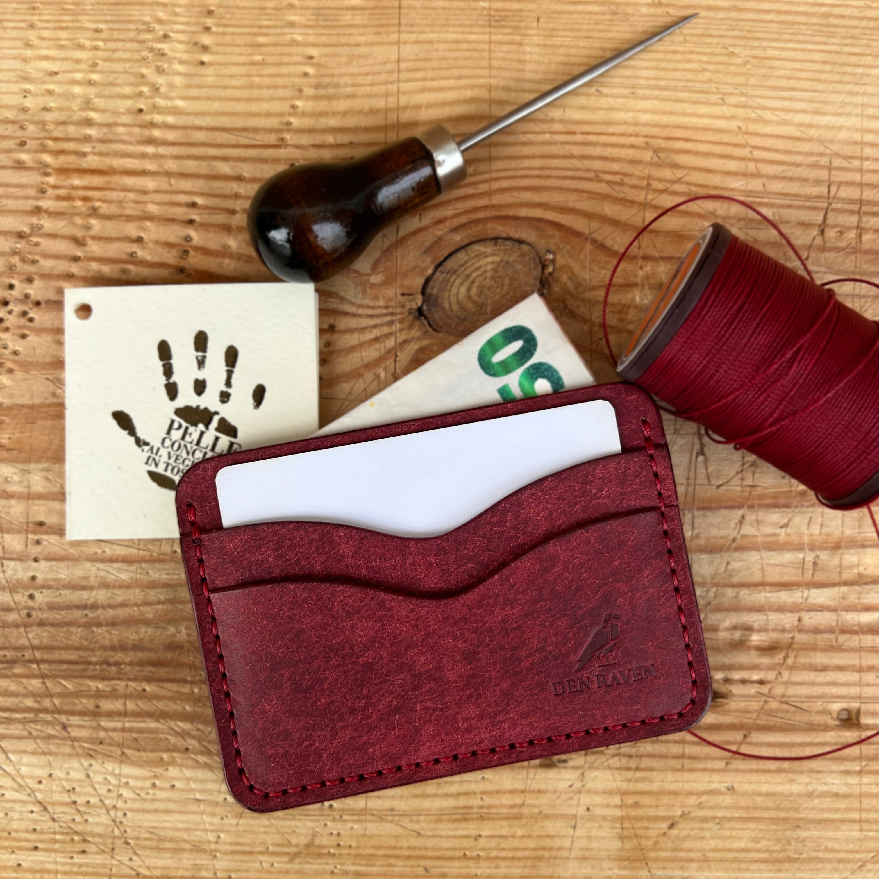 Red leather cardholder with sewing tools on a wooden surface