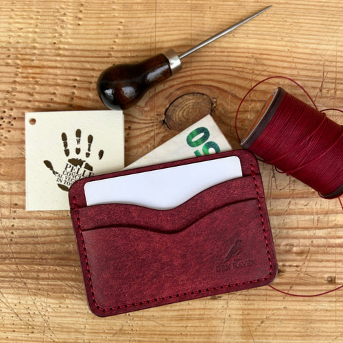Red leather cardholder with sewing tools on a wooden surface