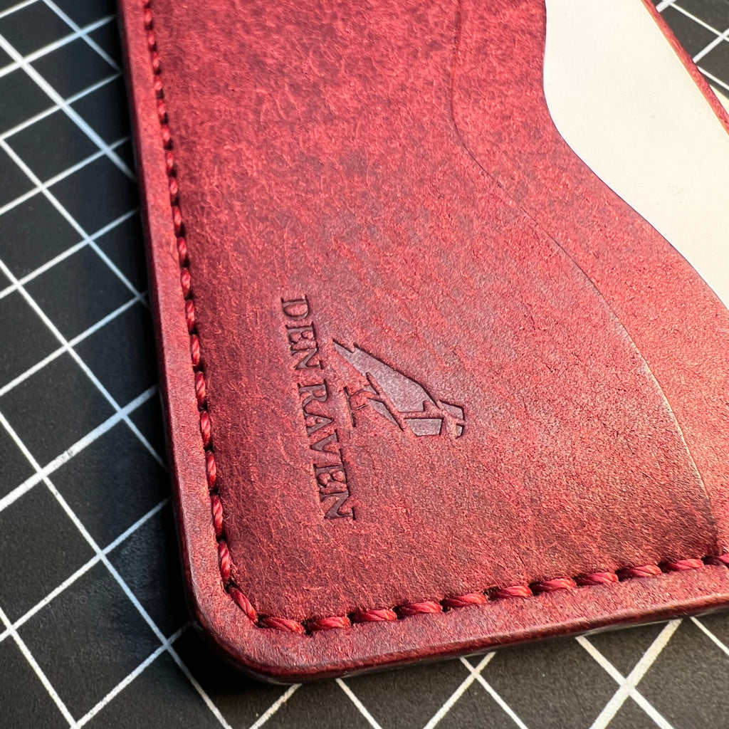Red leather cardholder with 'DenRaven' branding on a grid background