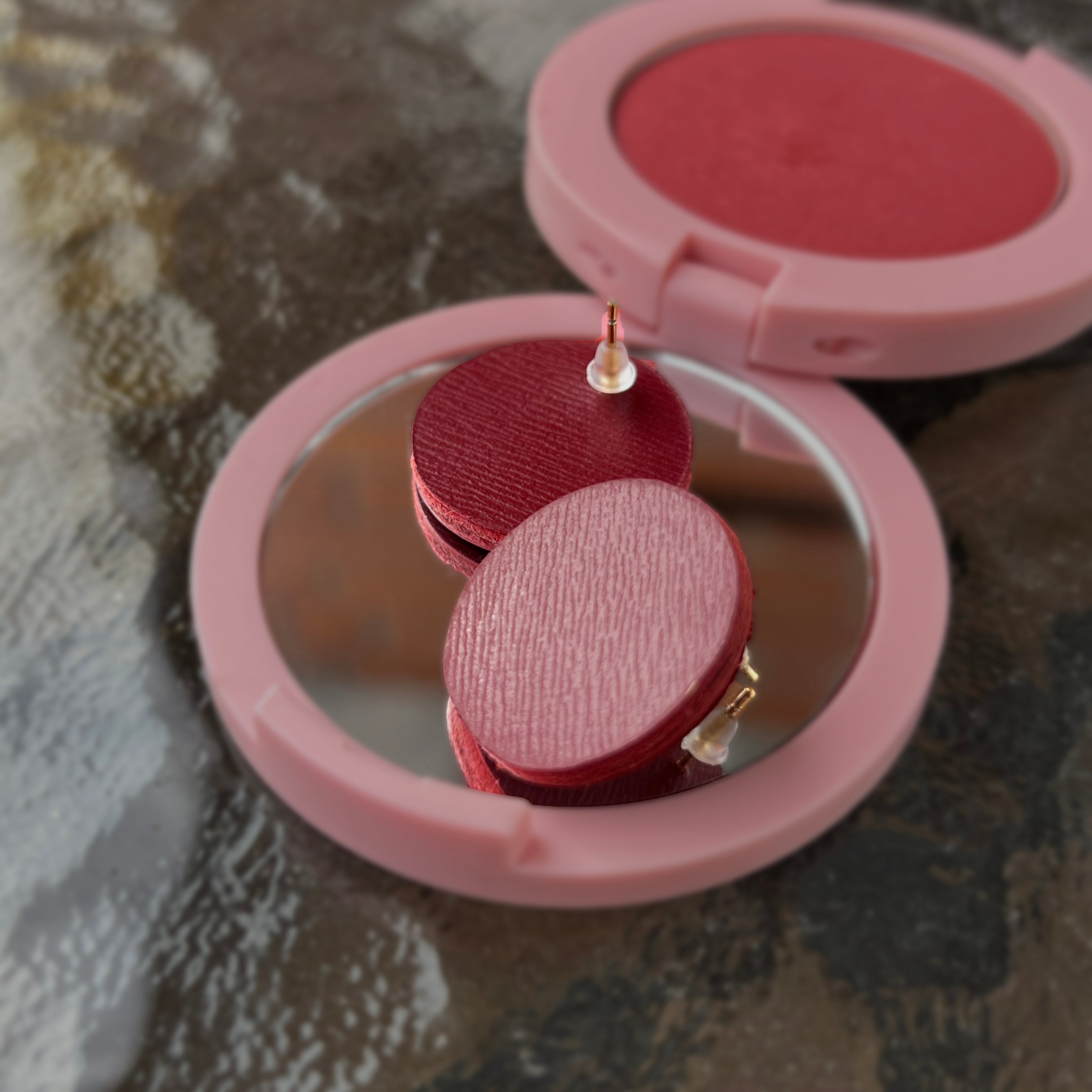 Pink earrings with a mirror on a textured surface