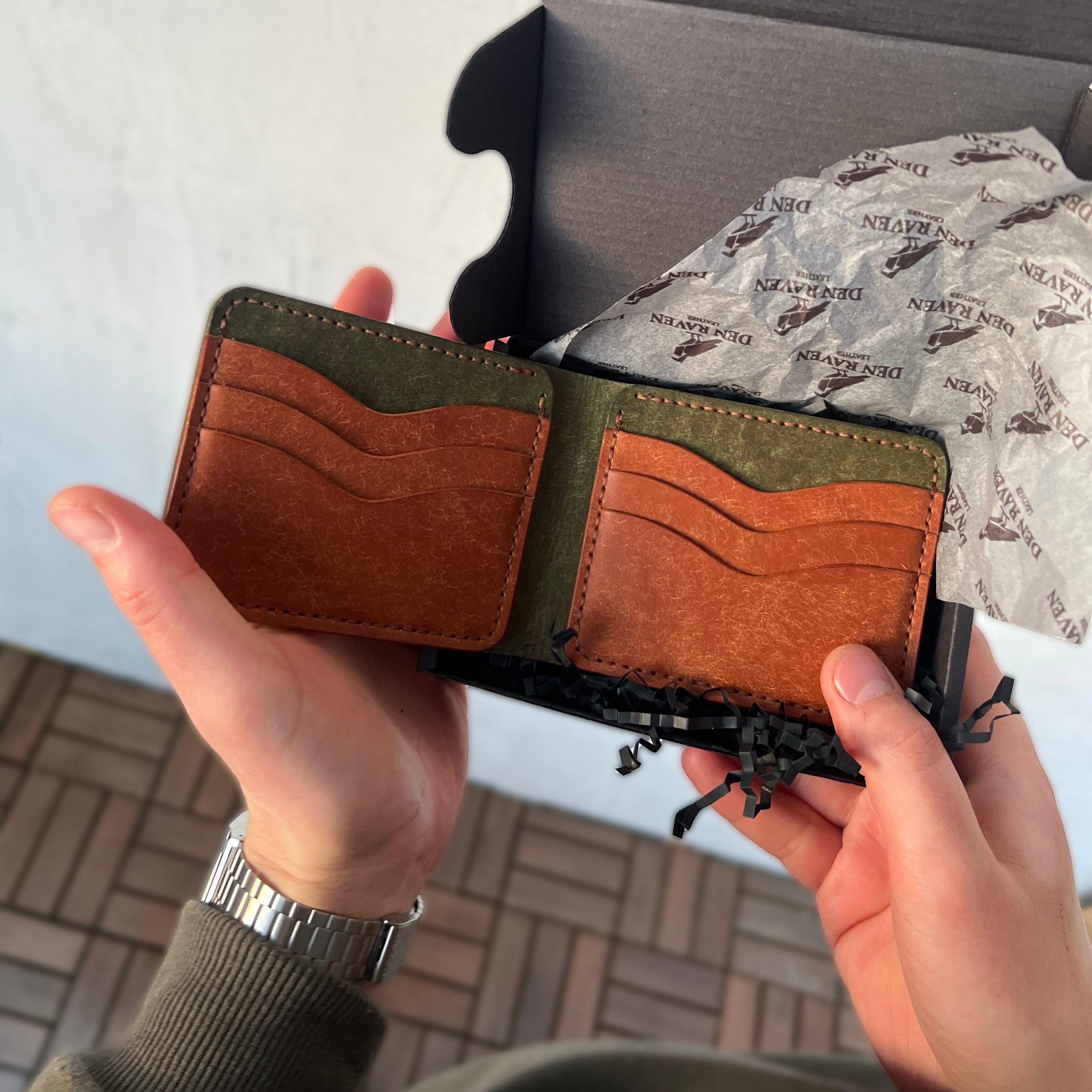 Person holding a brown and green wallet with a white background