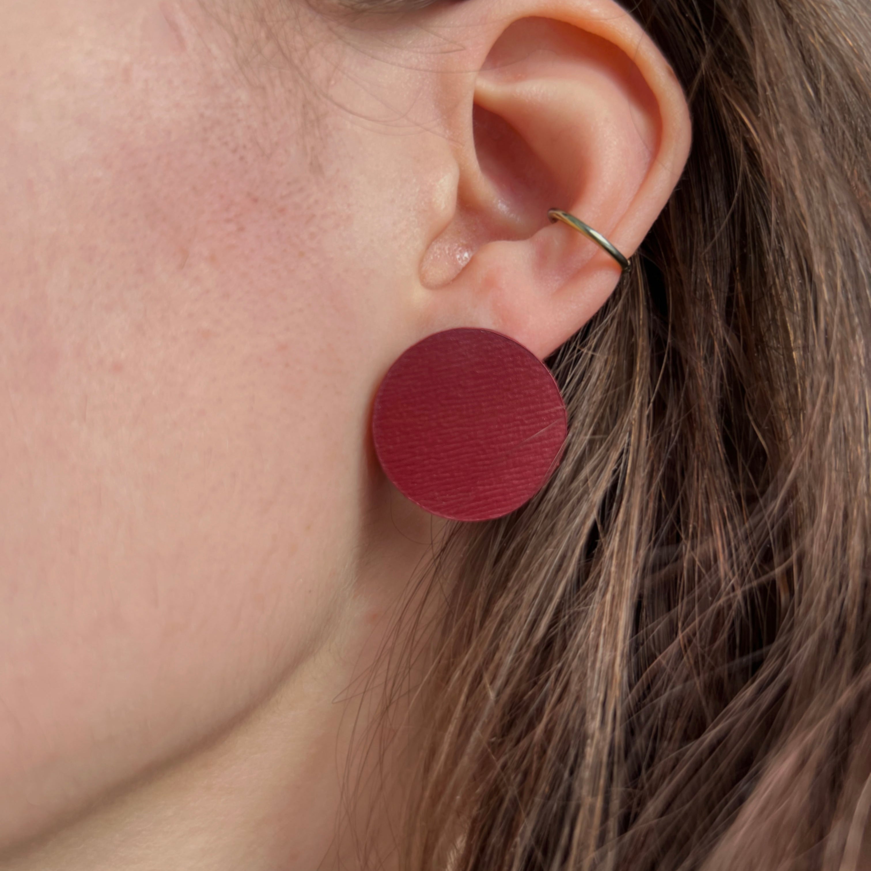 Close-up of an ear wearing a red circular earring with blurred background