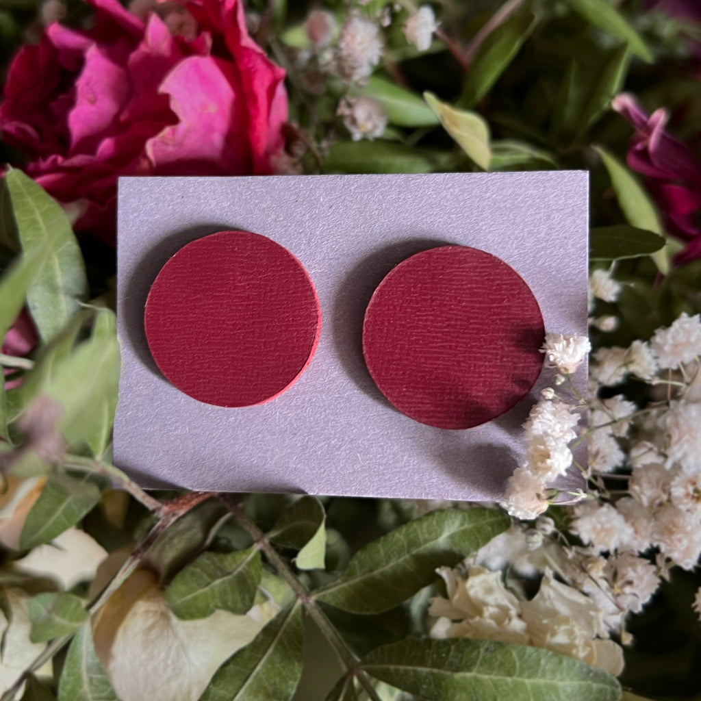 Red circular earrings on a card with flowers in the background