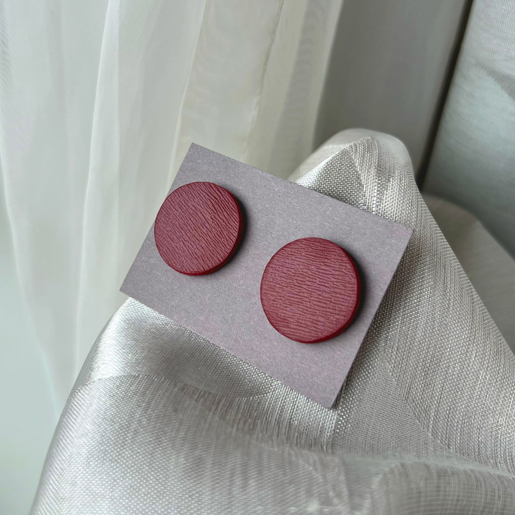 Pair of round wooden earrings on a gray card against a light fabric background