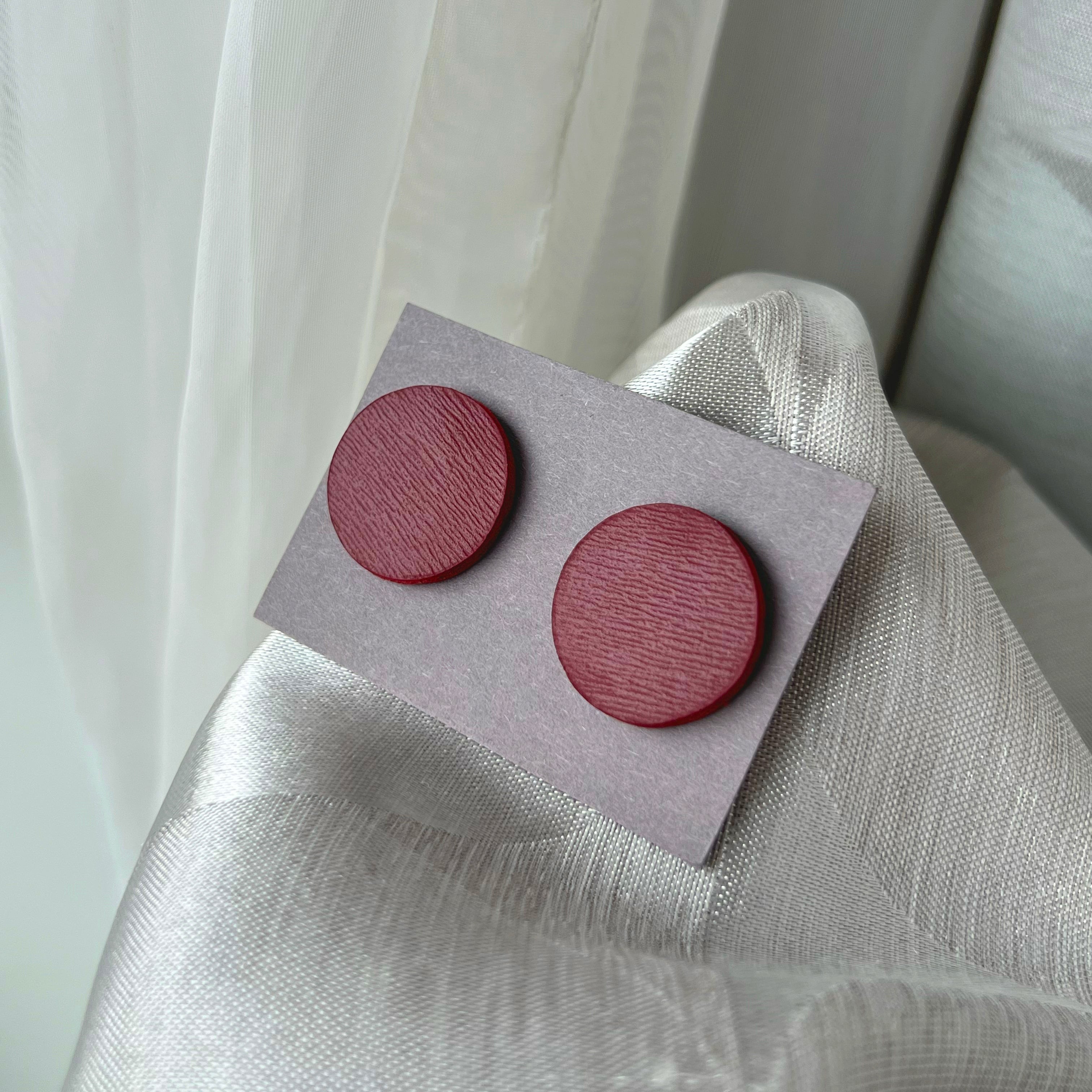 Pair of round wooden earrings on a gray card against a light fabric background