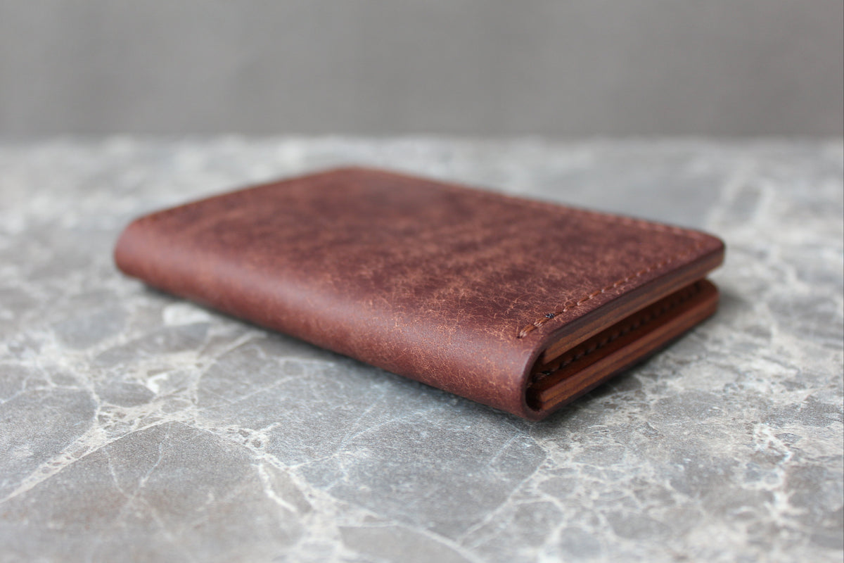 A brown leather card holder wallet with a distressed texture, resting on a gray marble surface.